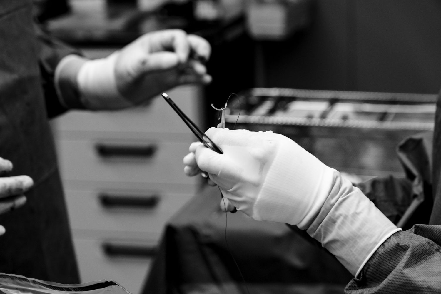 Gloved hands holding surgical scissors during a medical procedure in a clinical setting.