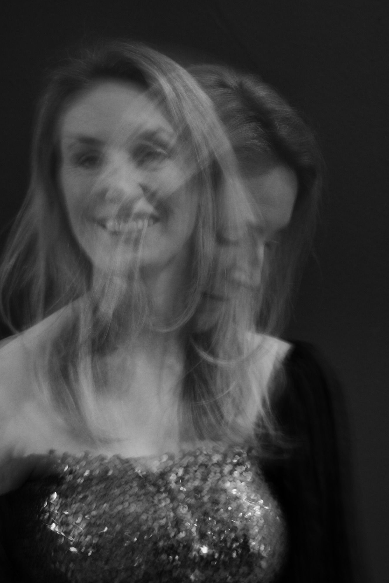 Artistic blurred black and white portrait of a smiling woman in a sequined dress against dark background.