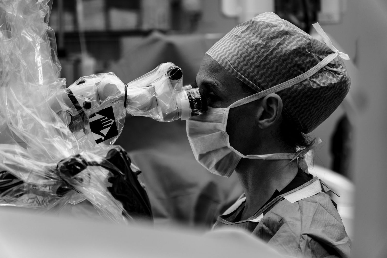 Black and white profile shot of a masked surgeon looking through surgical loupes during an operation. Documentary photography by Constanze A