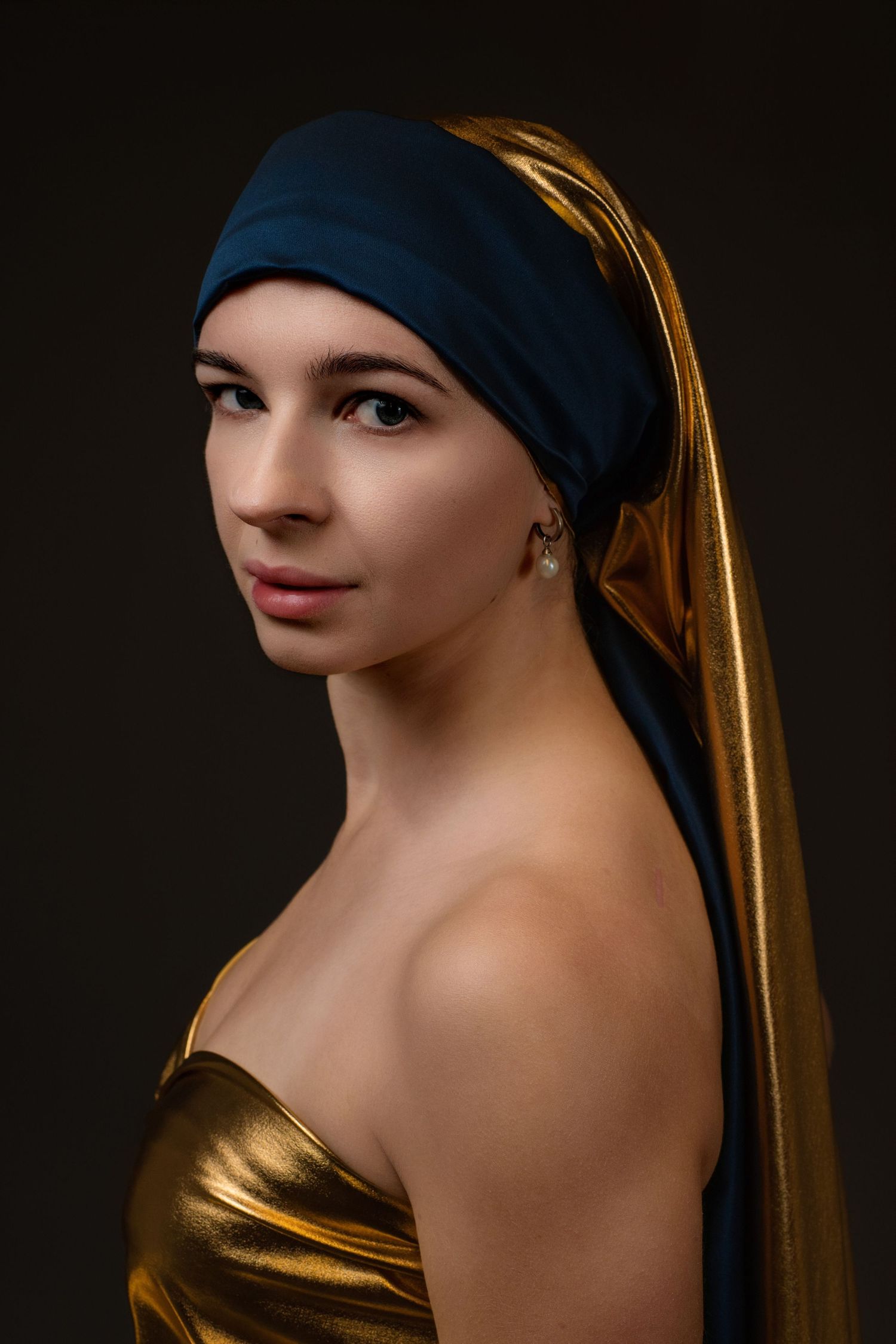 Young woman in gold dress and blue-gold turban with pearl earring, inspired by Vermeer painting, dark background.