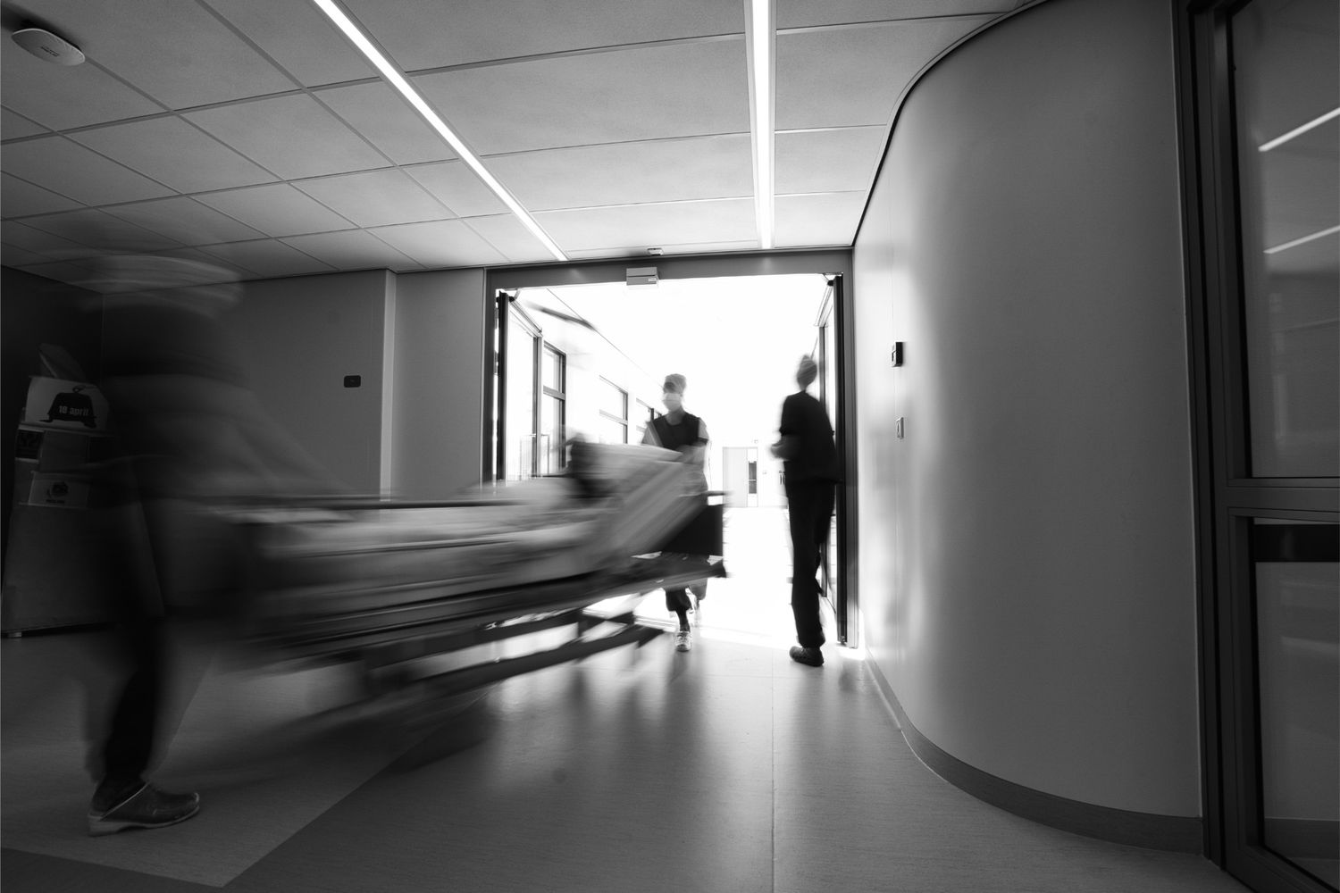 Black and white motion blur photo of hospital staff rushing a patient on a gurney through a hospital corridor.