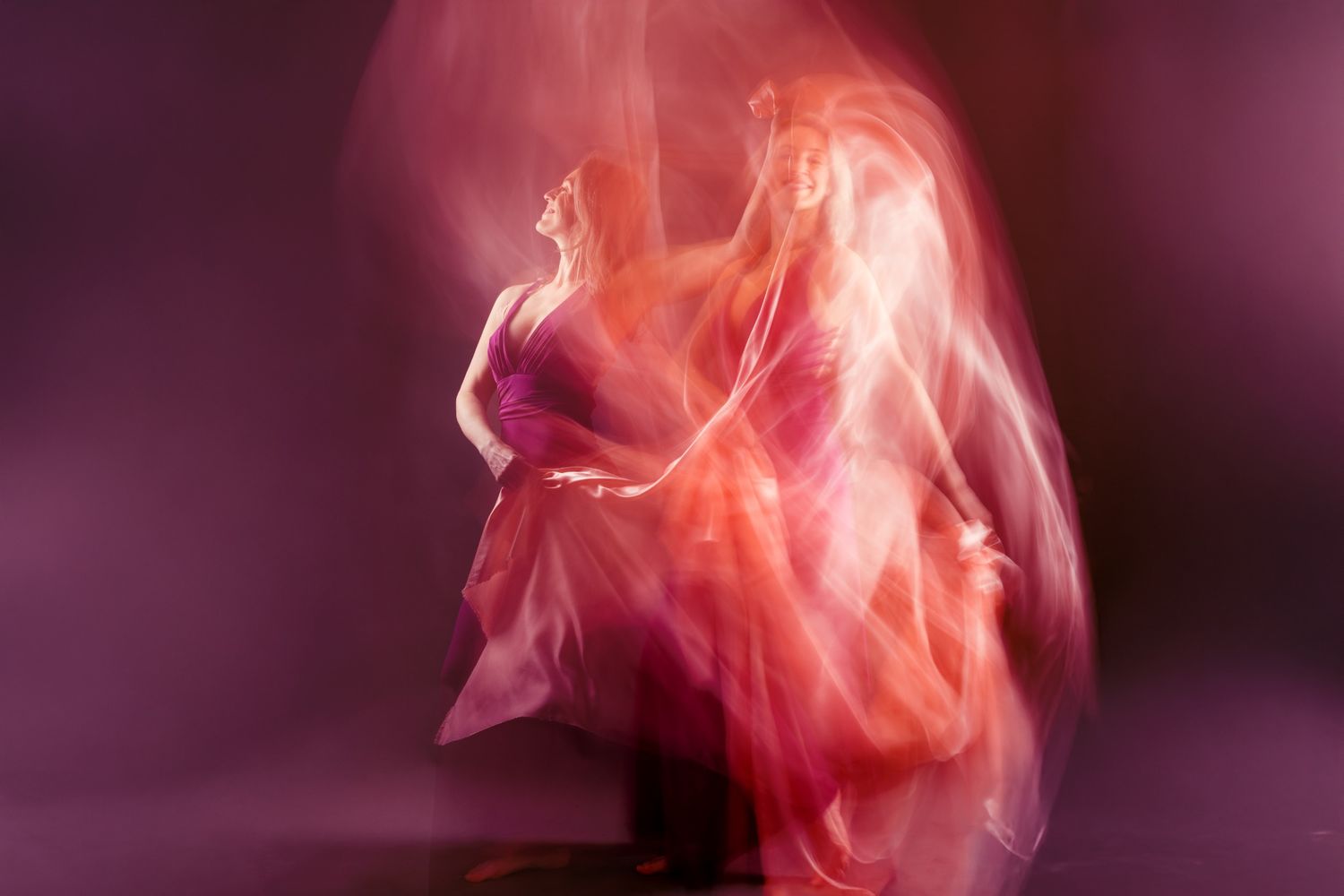 Blurred motion photo of a woman in flowing pink and red dress dancing against a purple background.