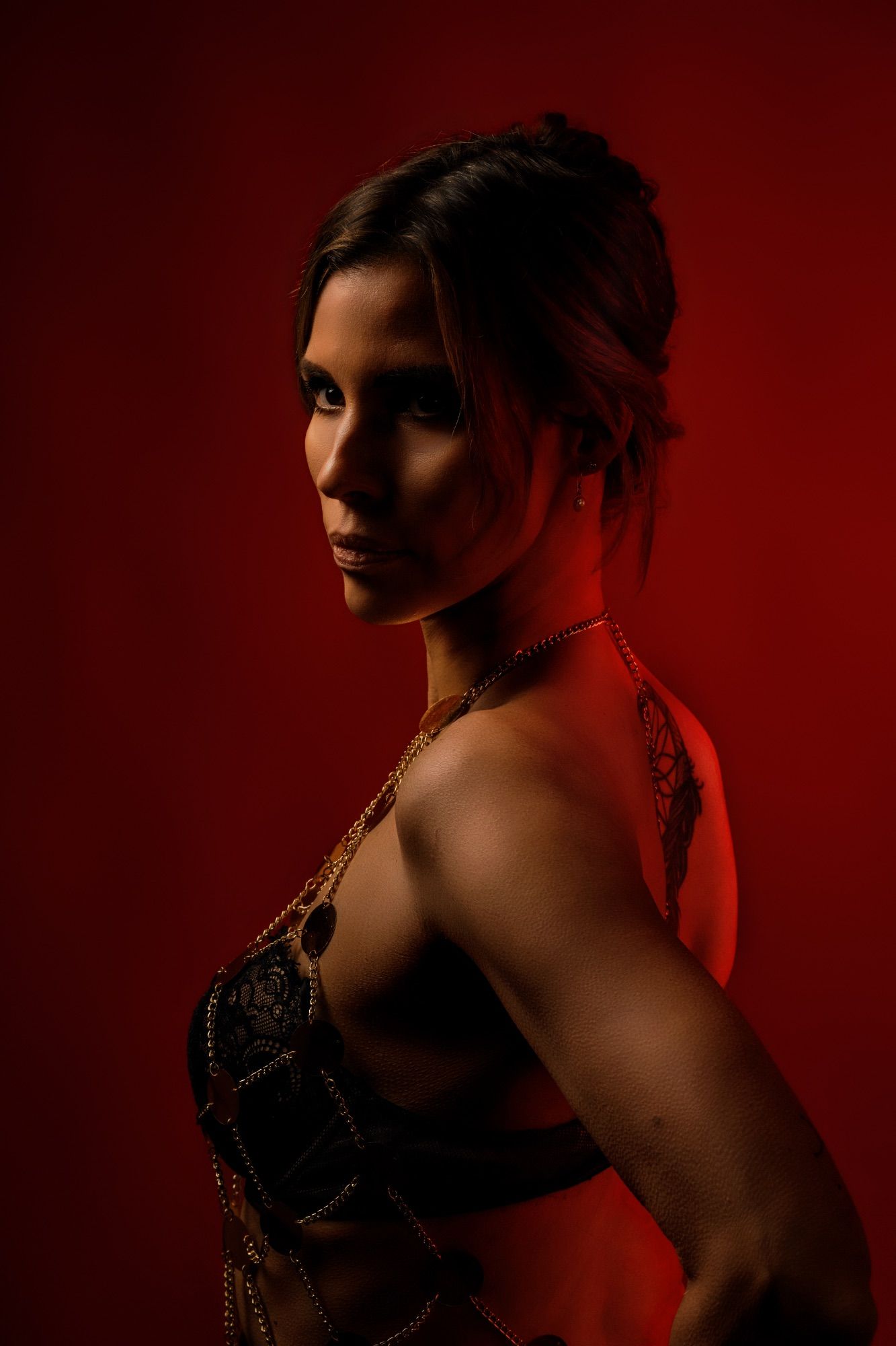 A woman in an ornate gold and black costume poses against a dramatic red background with moody lighting.