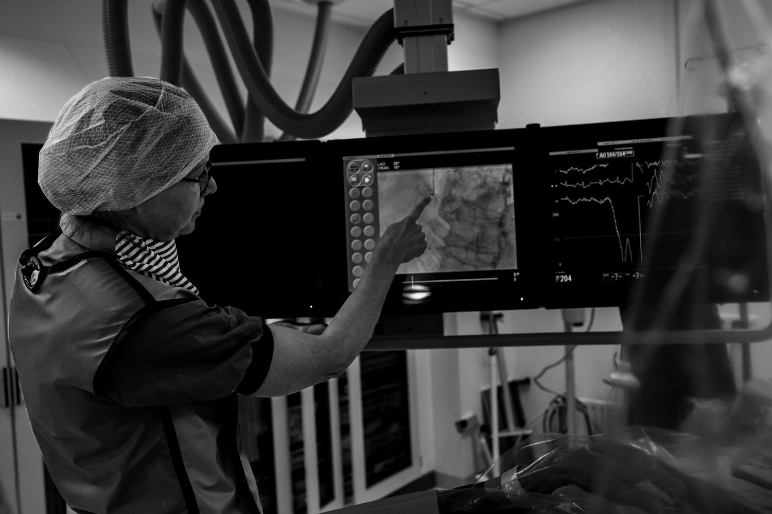 Medical professional in surgical cap analyzes patient data on monitors in a hospital operating room.