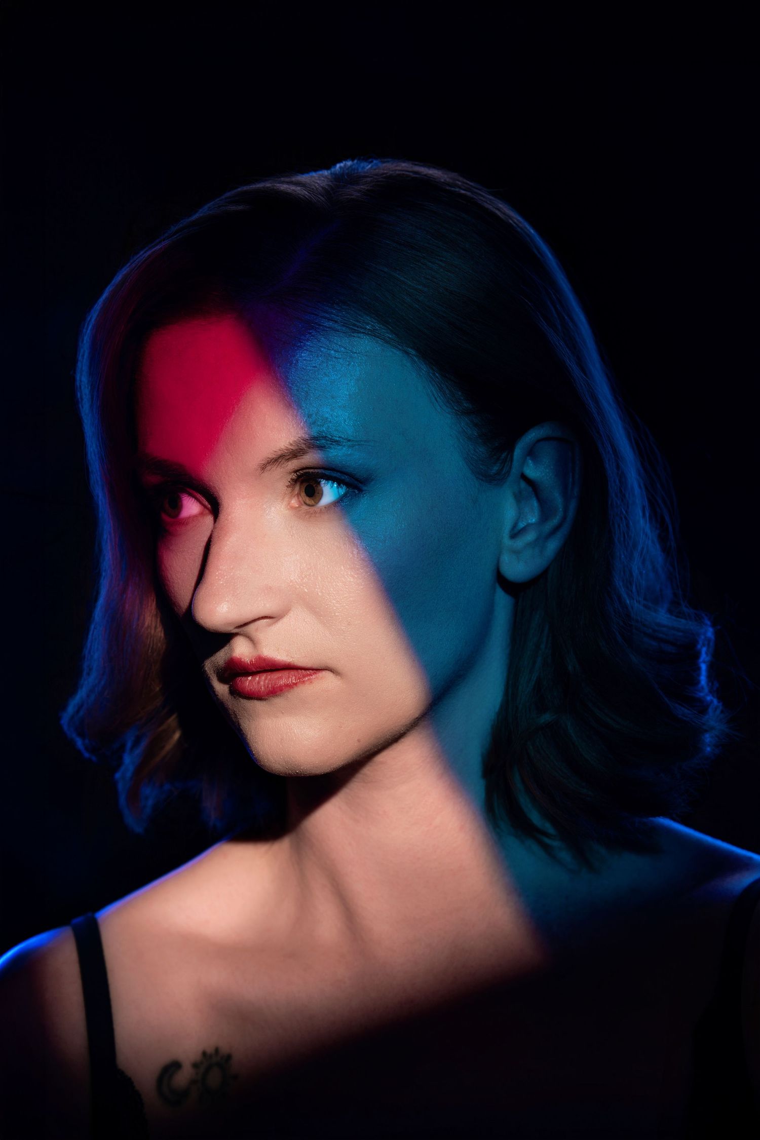 Dramatic studio portrait of woman with split red and blue neon lighting on dark background.