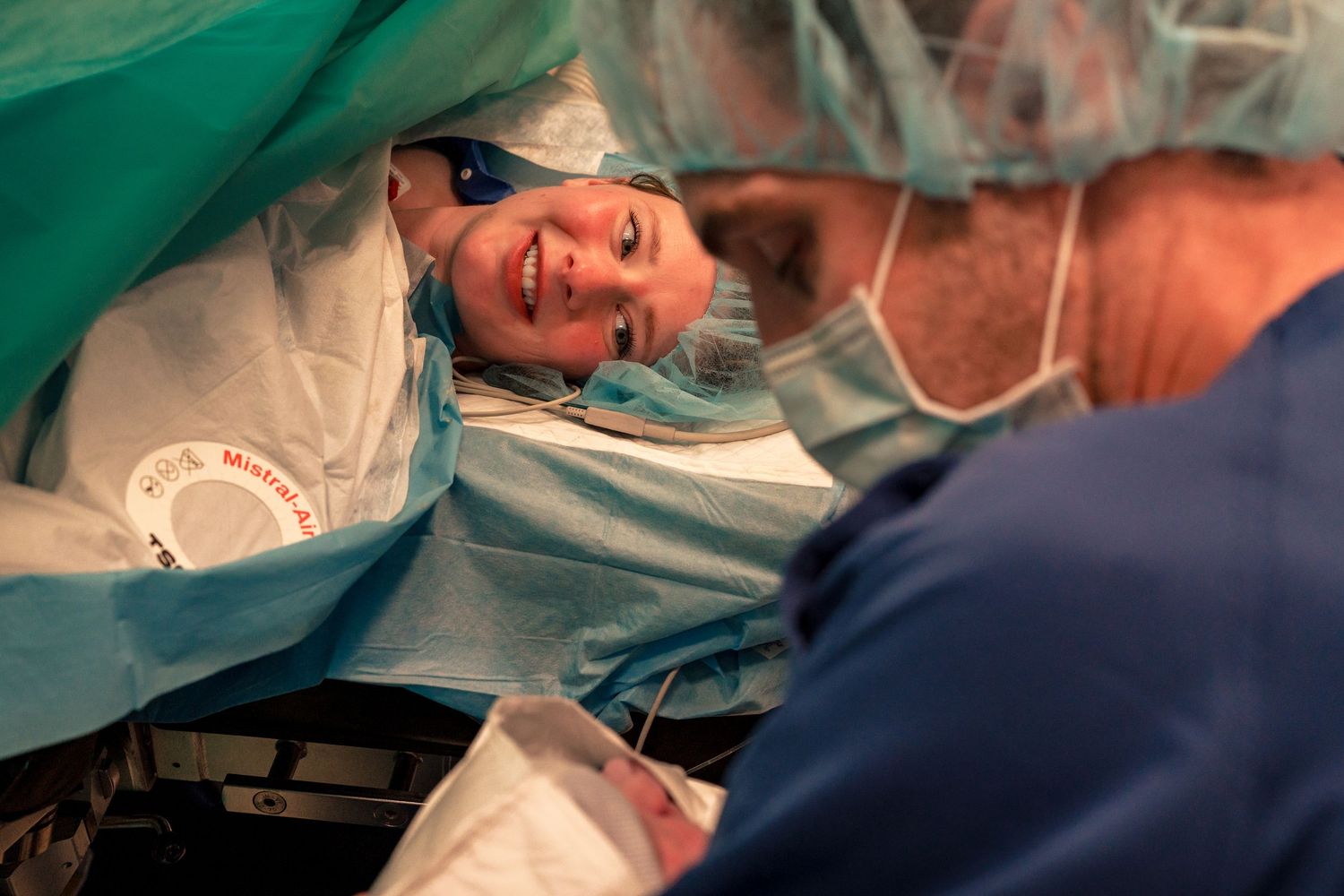 Smiling mother lying on operating table during cesarean section delivery procedure. Birth photography by Constanze Ariane