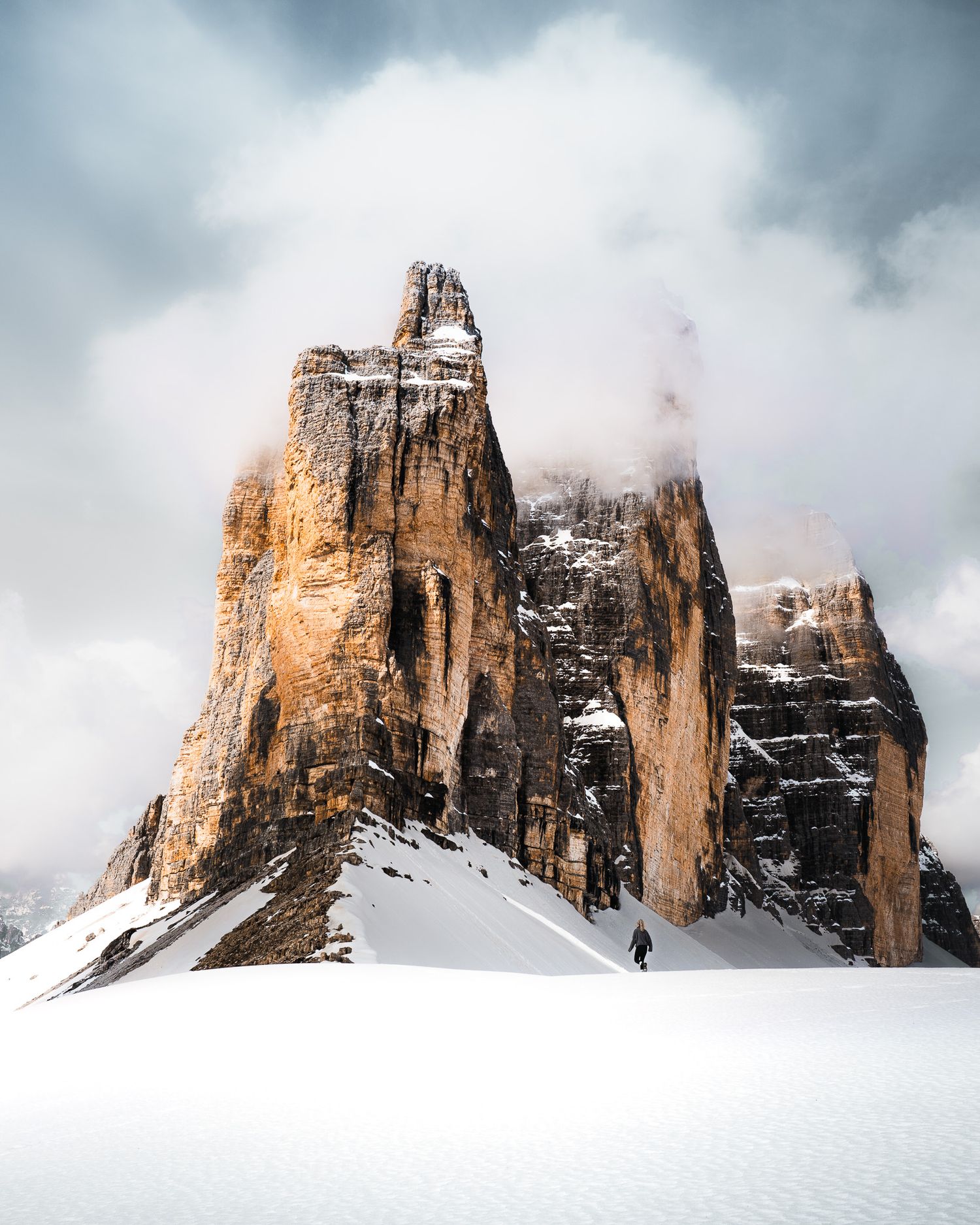 Eine abenteuerliche Aufnahme von den Drei Zinnen, Dolomiten im Schnee. Eine Person wandert im Vordergrund.