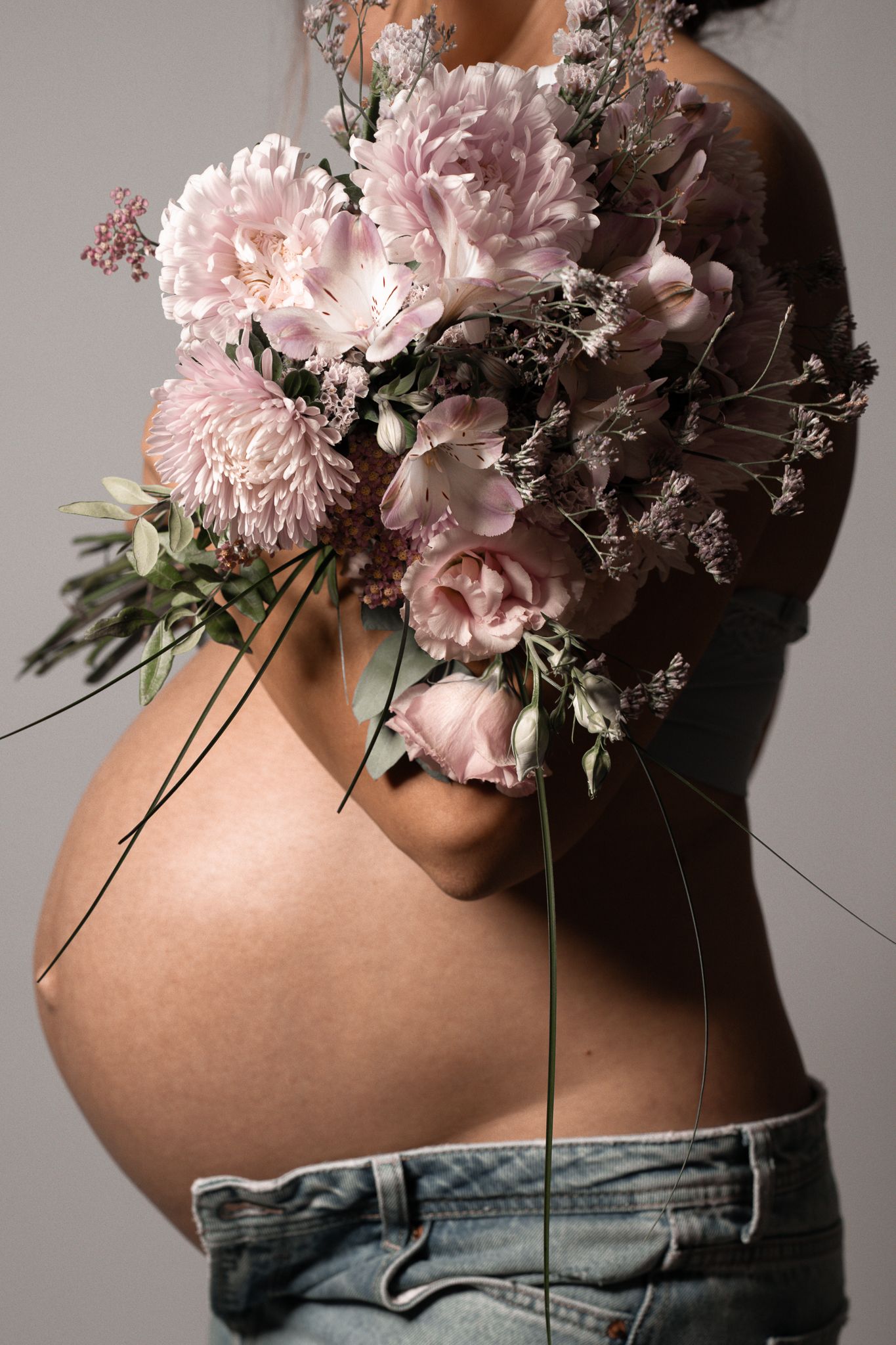 Eine kreative Fotografie einer Schwangeren, die einen großen Blumenstrauß vor sich im Arm hält um ihren Bauch zu schmücken.