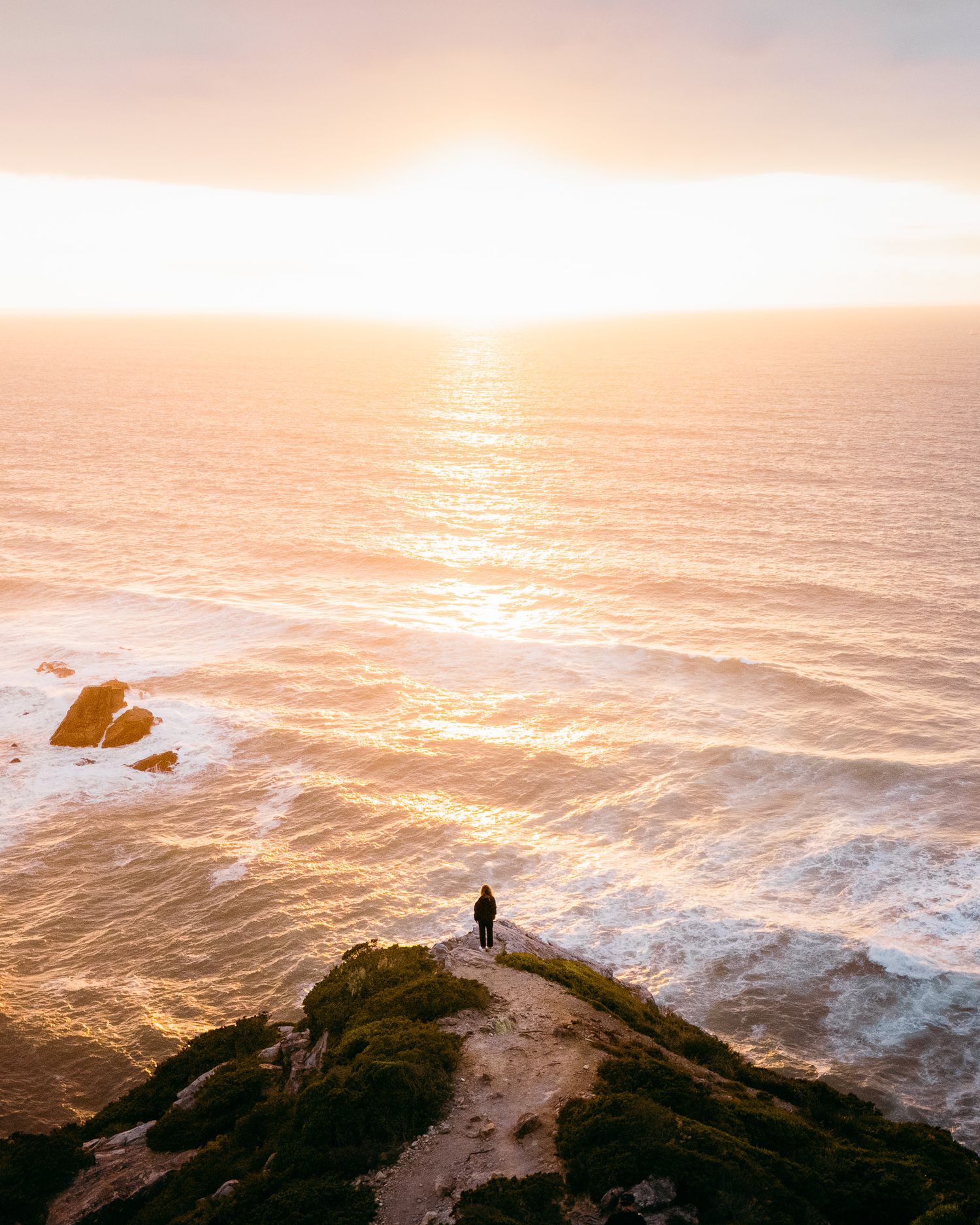 Eine tolle Aussicht auf das Meer bei Sonnenuntergang. Eine Person steht auf einem Felsvorsprung und schaut auf den Horizont.