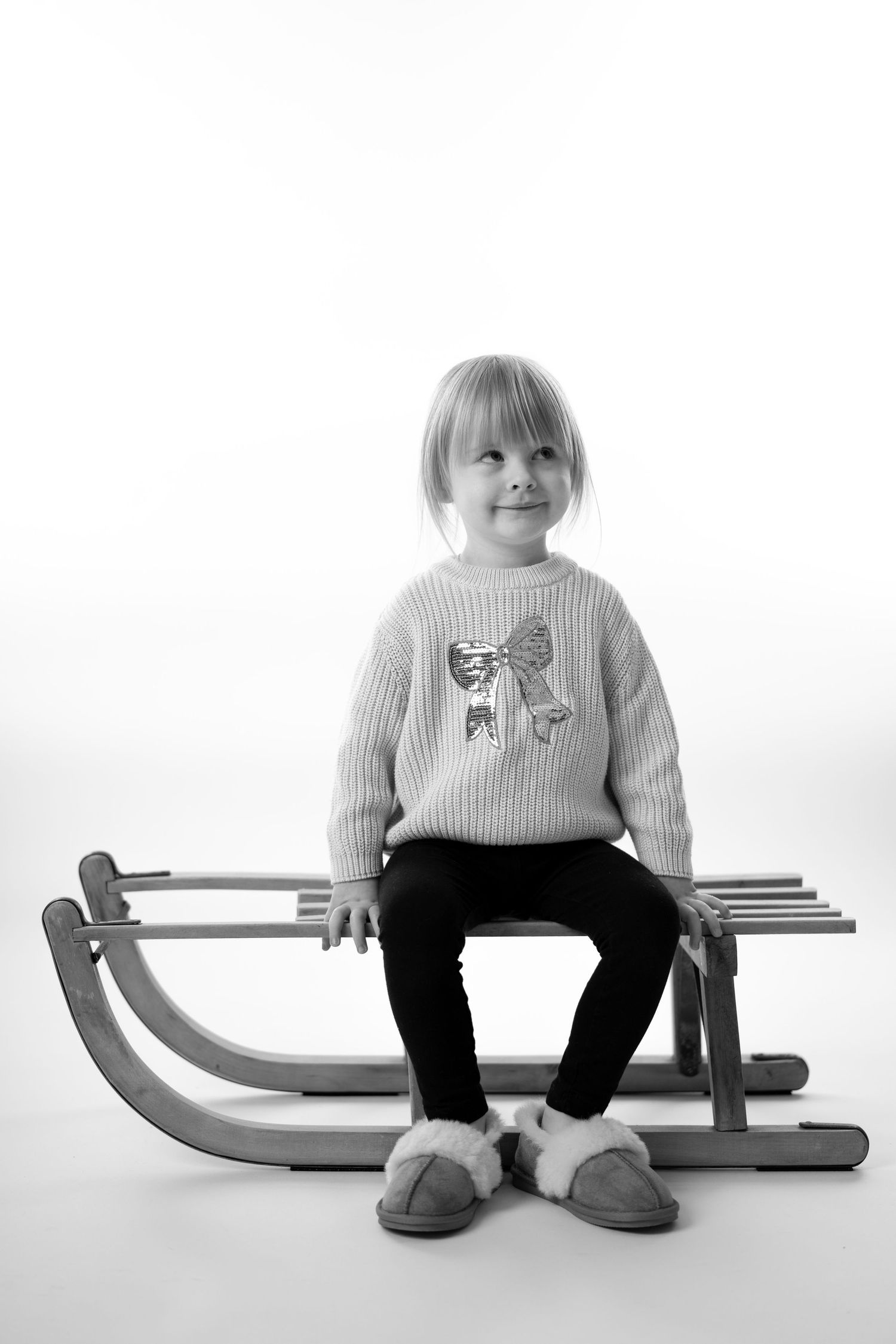 Eine Fotografie von einem Kleinkind, dass auf einem Schlitten sitzt und verschmitzt schaut. Kreative schwarz-weiß Portraitfotografie