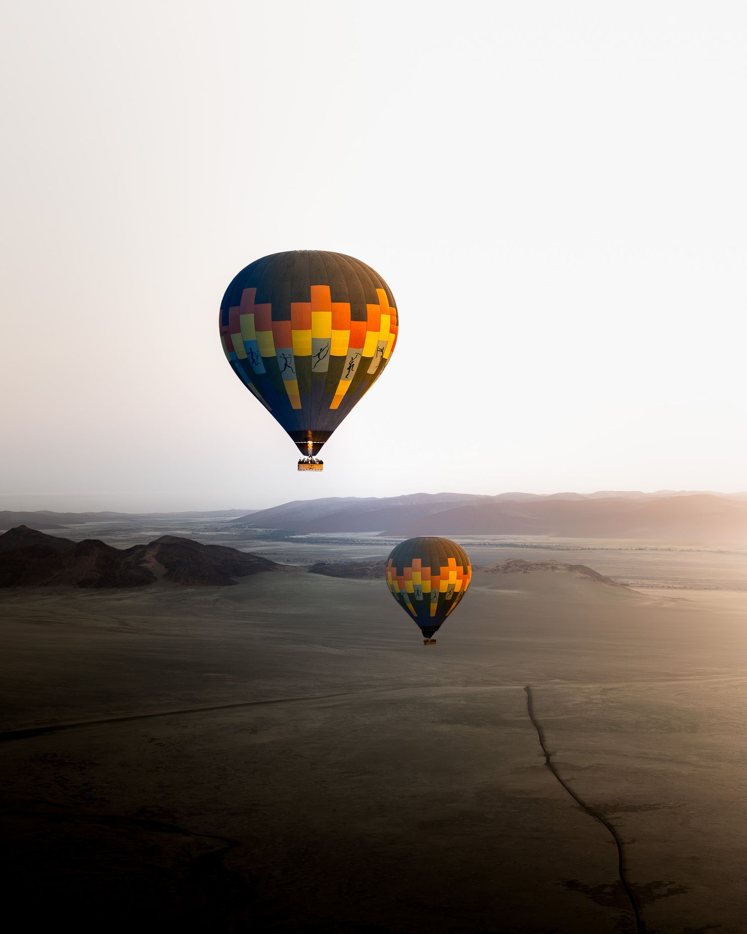 Zwei bunte Heißluftballons in der Namib Wüste, schweben hoch über dem Boden im Sonnenaufgang.