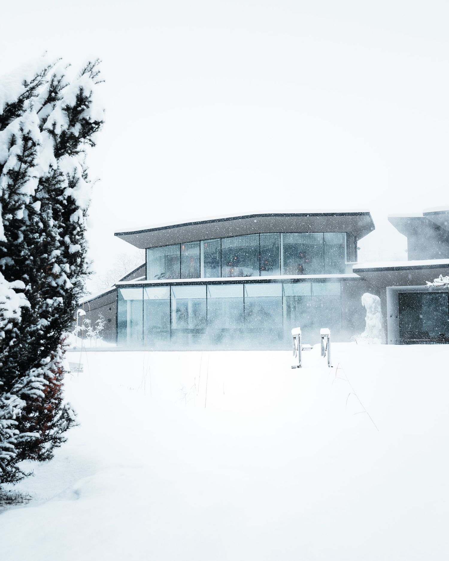 Ein Wellnesshotel im Schnee mit großer moderner Glasfassade. Der Pool davor ist zugeschneit, sodass nur der Einstieg zu sehen ist.