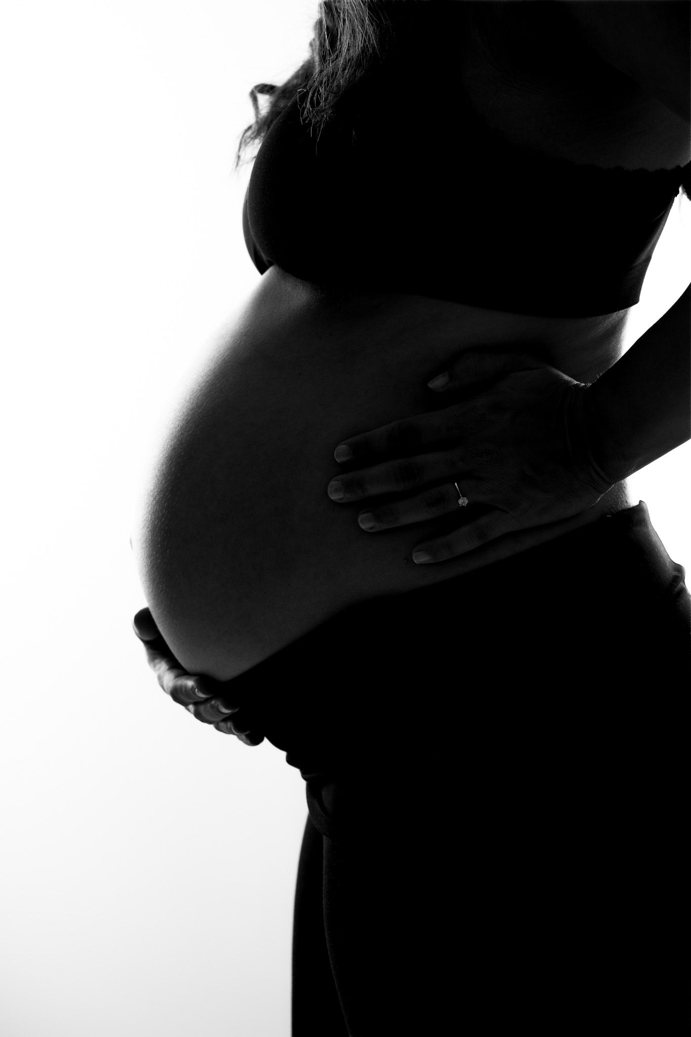 Stilvolle High Key Fotografie von einem Babybauch. Man sieht nur die Silhouette der Frau in Schwarz vor einem Leuten weißen Hintergrund.