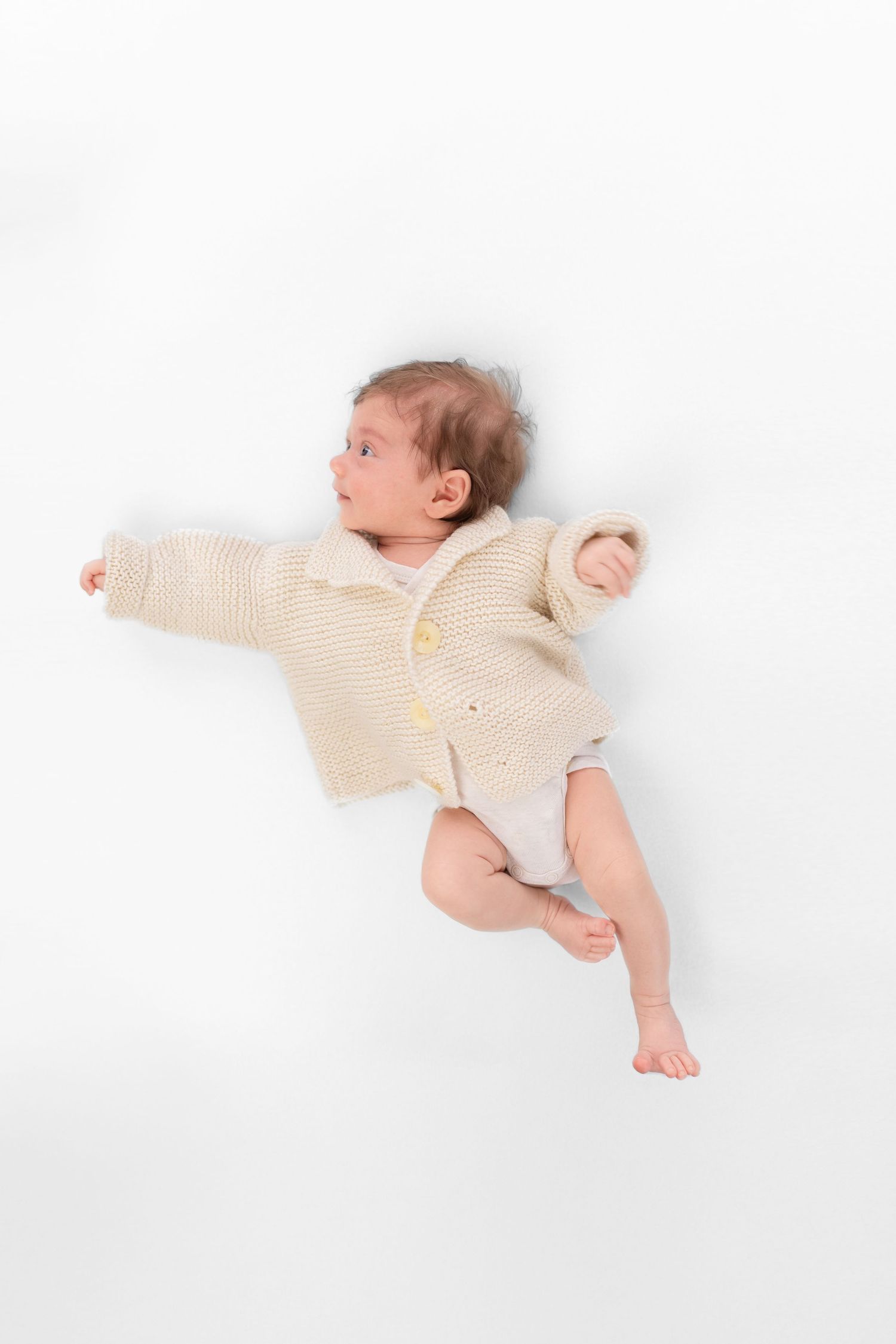 Auf dem Foto ist ein Neugeborenes zu sehen, dass ein Strickpullover trägt und zur Seite schaut. Stilvolle, liebevolle Babyfotografie