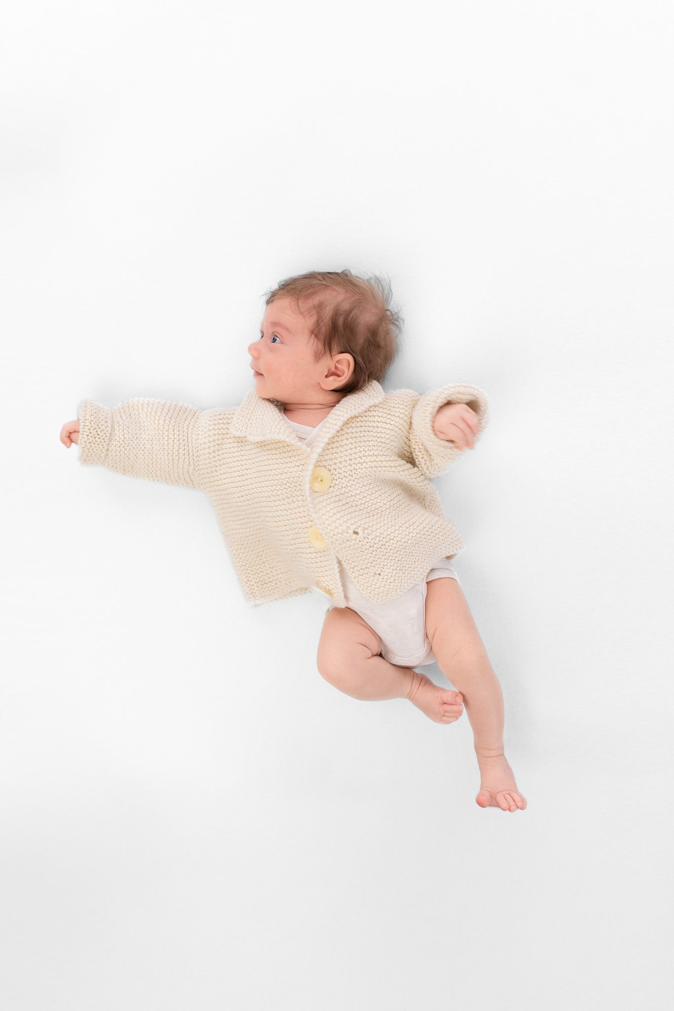 Auf dem Foto ist ein Neugeborenes zu sehen, dass ein Strickpullover trägt und zur Seite schaut. Stilvolle, liebevolle Babyfotografie