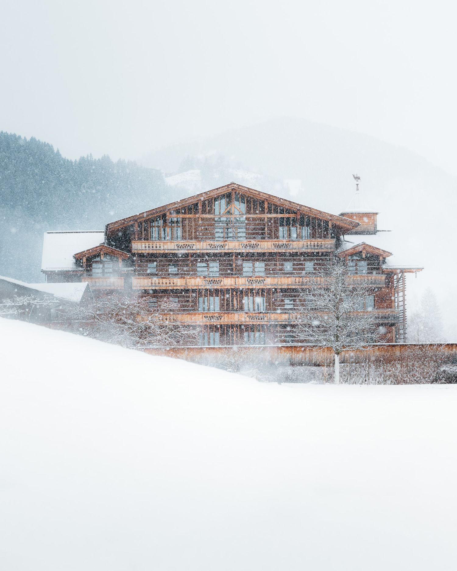 Ein Hotel mit Holzfassade aus der Ferne fotografiert. Der Schnee umhüllt die Landschaft drum herum und erzeugt eine gemütliche Stimmung.