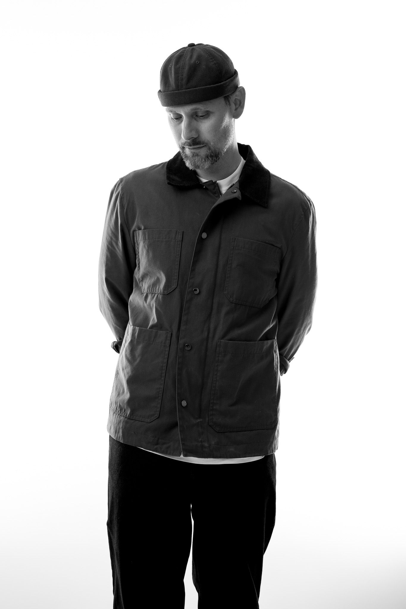 High key Portrait in schwarz-weiß von einem jungen Mann, der vor sich auf den Boden schaut, die Arme hinter dem Rücken.
