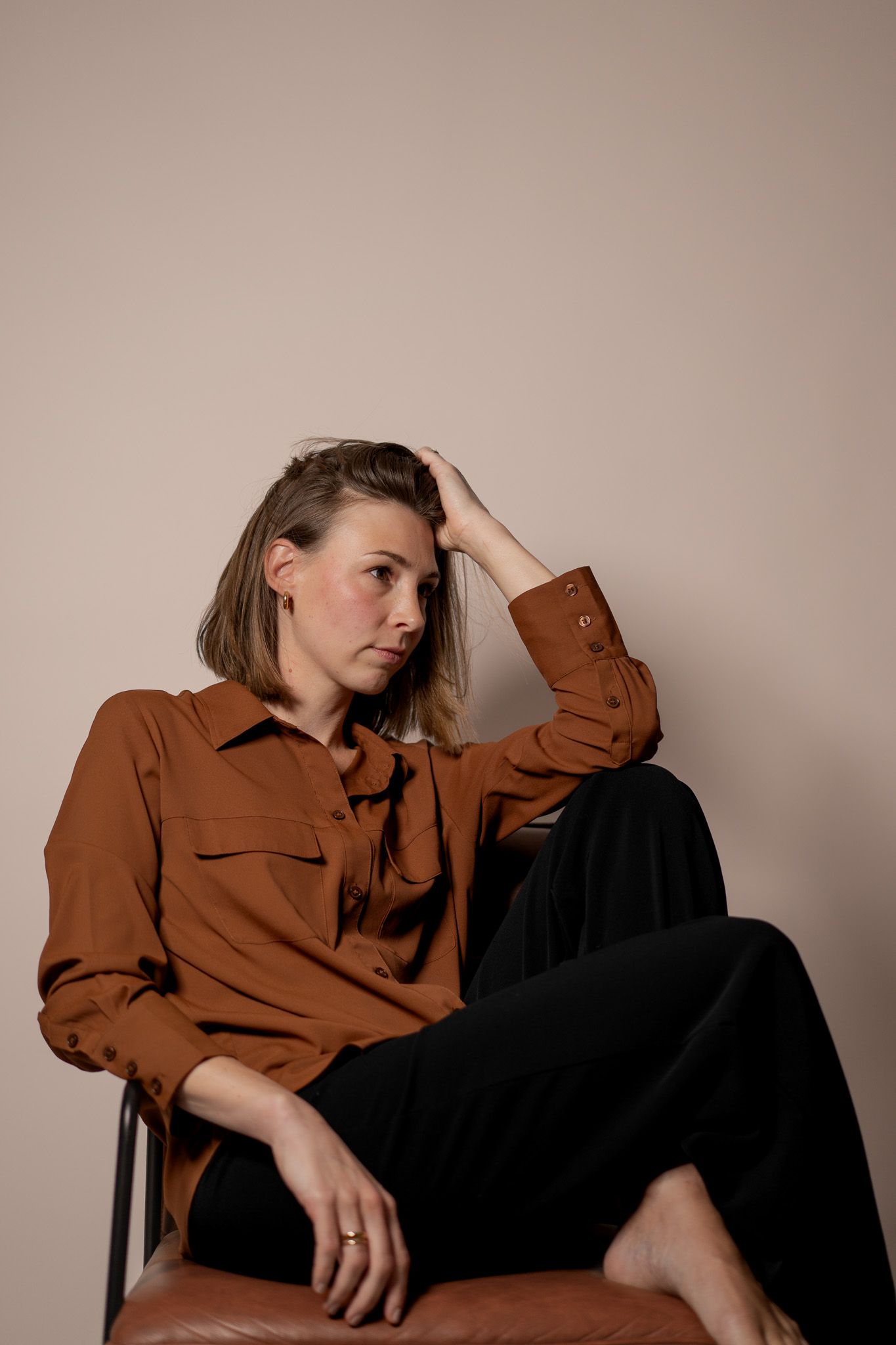 Eine Frau sitzt auf einem Stuhl und posiert für ein Portrait Foto. Sie stützt den Kopf ab und schaut zur Seite. Warme Farben.