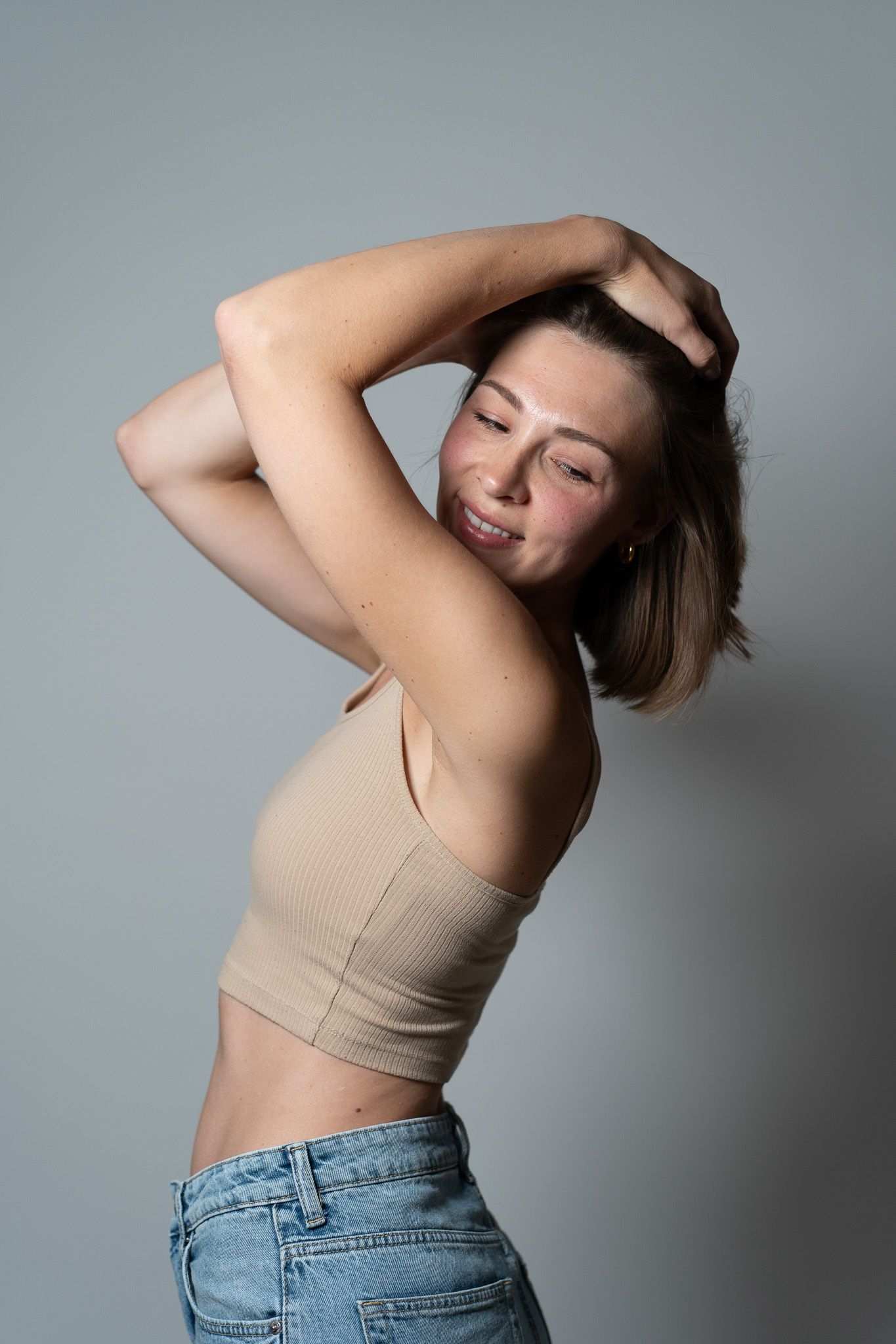 Ein fröhliches dynamisches Portrait einer jungen Frau die sich mit beiden Händen durch die Haare fährt und dabei lächelnd zur Seite schaut.