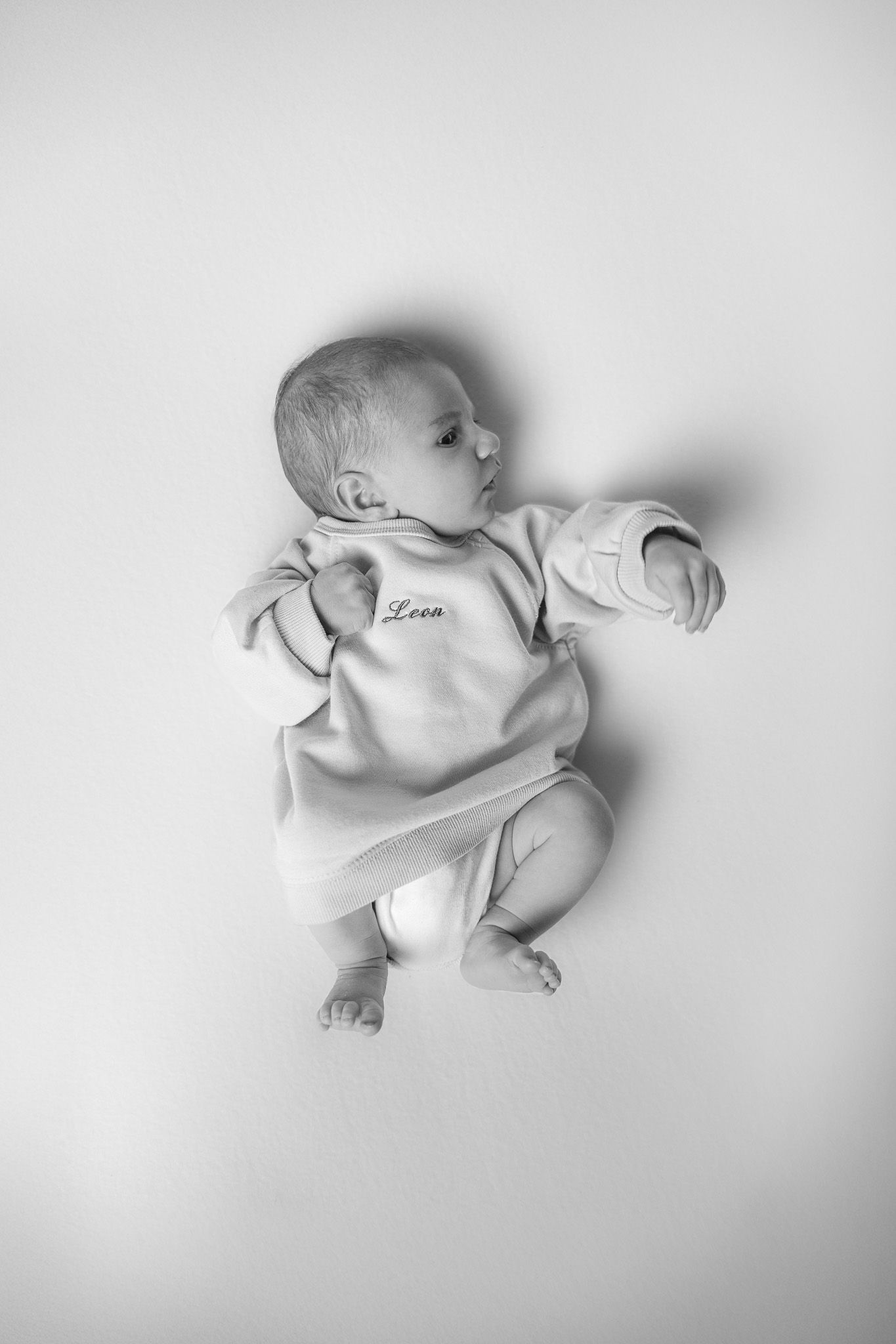 ein Portrait von einem Neugeborenen in schwarz weiß von oben. Das Baby liegt auf dem Rücken und hat einen Pullover an.
