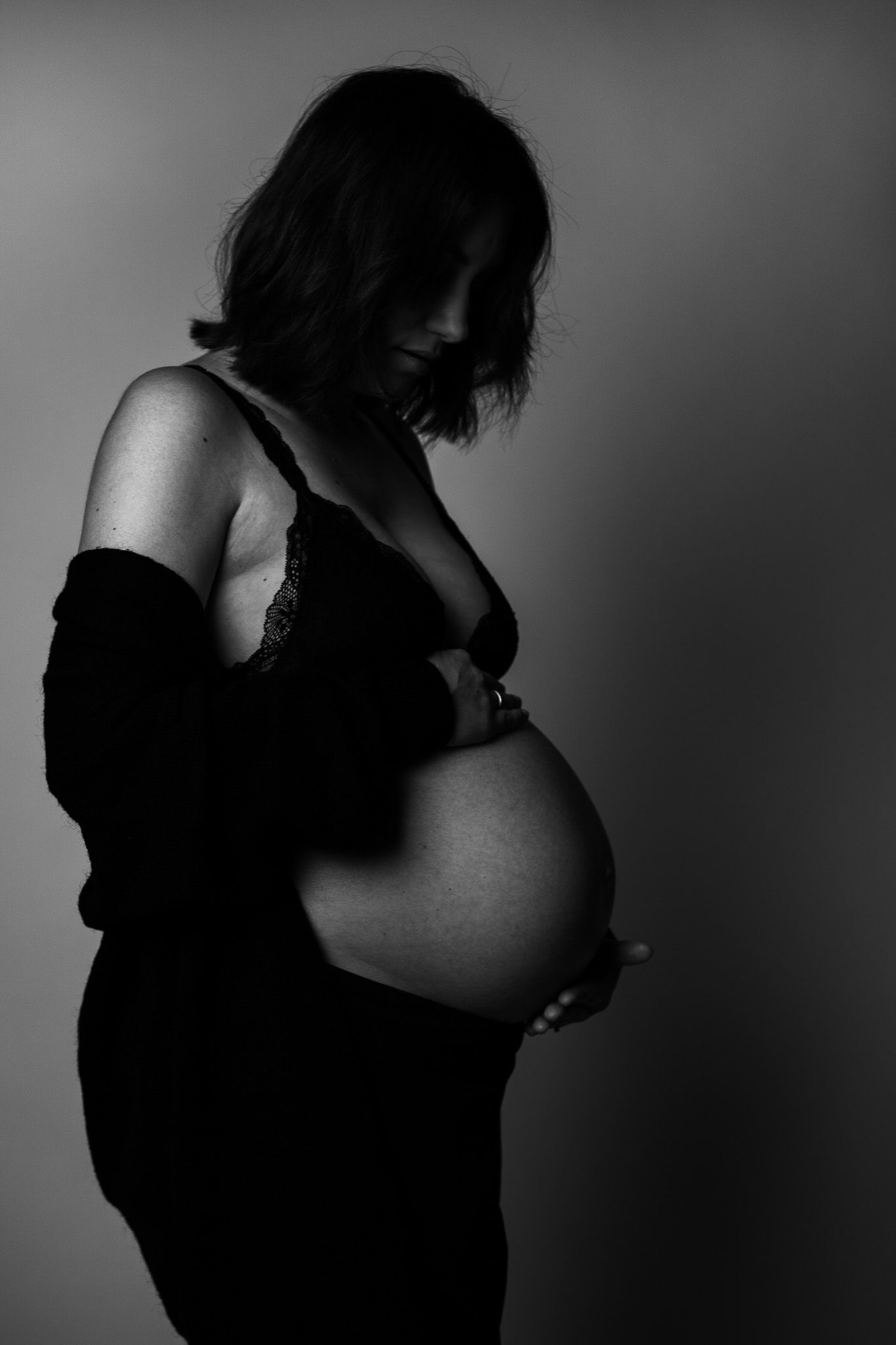 dunkle schwarz-weiß Fotografie einer Schwangeren im Profil die hinunter auf ihren Bauch schaut, das Gesicht von ihren Haaren verdeckt.