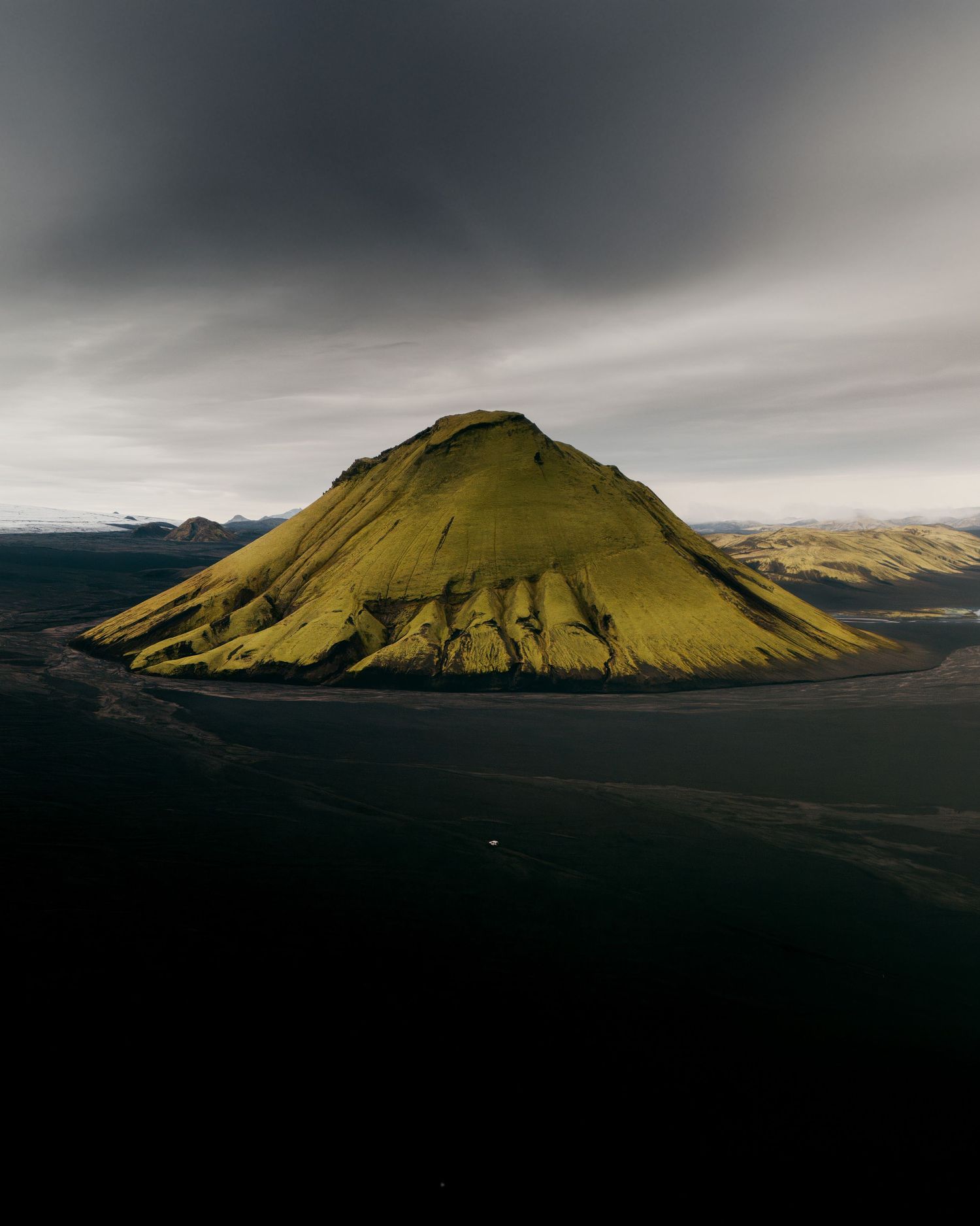 Eine spannende Landschaftsaufnahme von einem grünen Vulkan auf schwarzem Sand in Island.