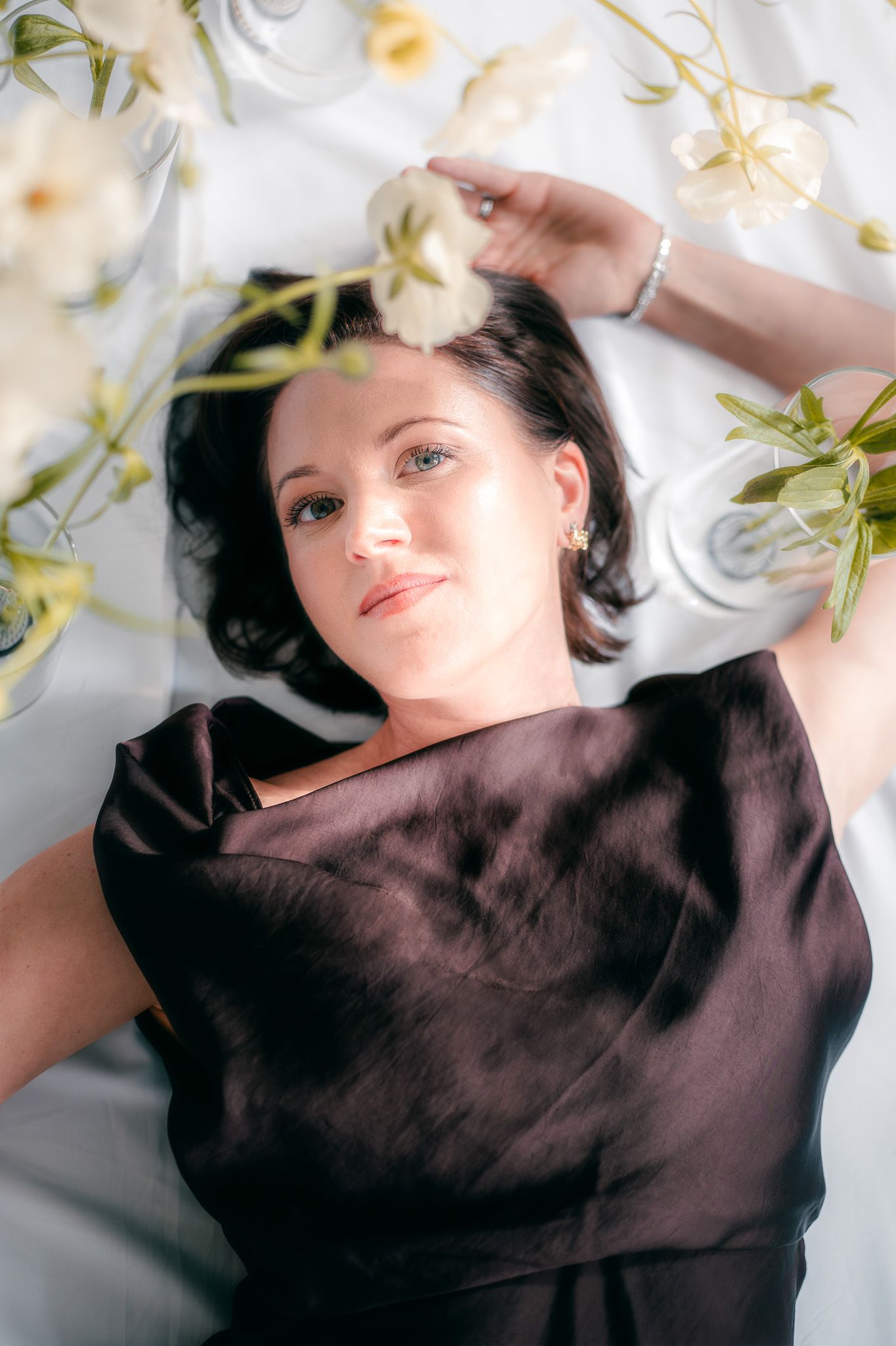 Ein künstlerisches Portrait von einer jungen Frau, die auf dem Rücken auf dem Boden zwischen Frühlingsblumen liegt und verträumt schaut.