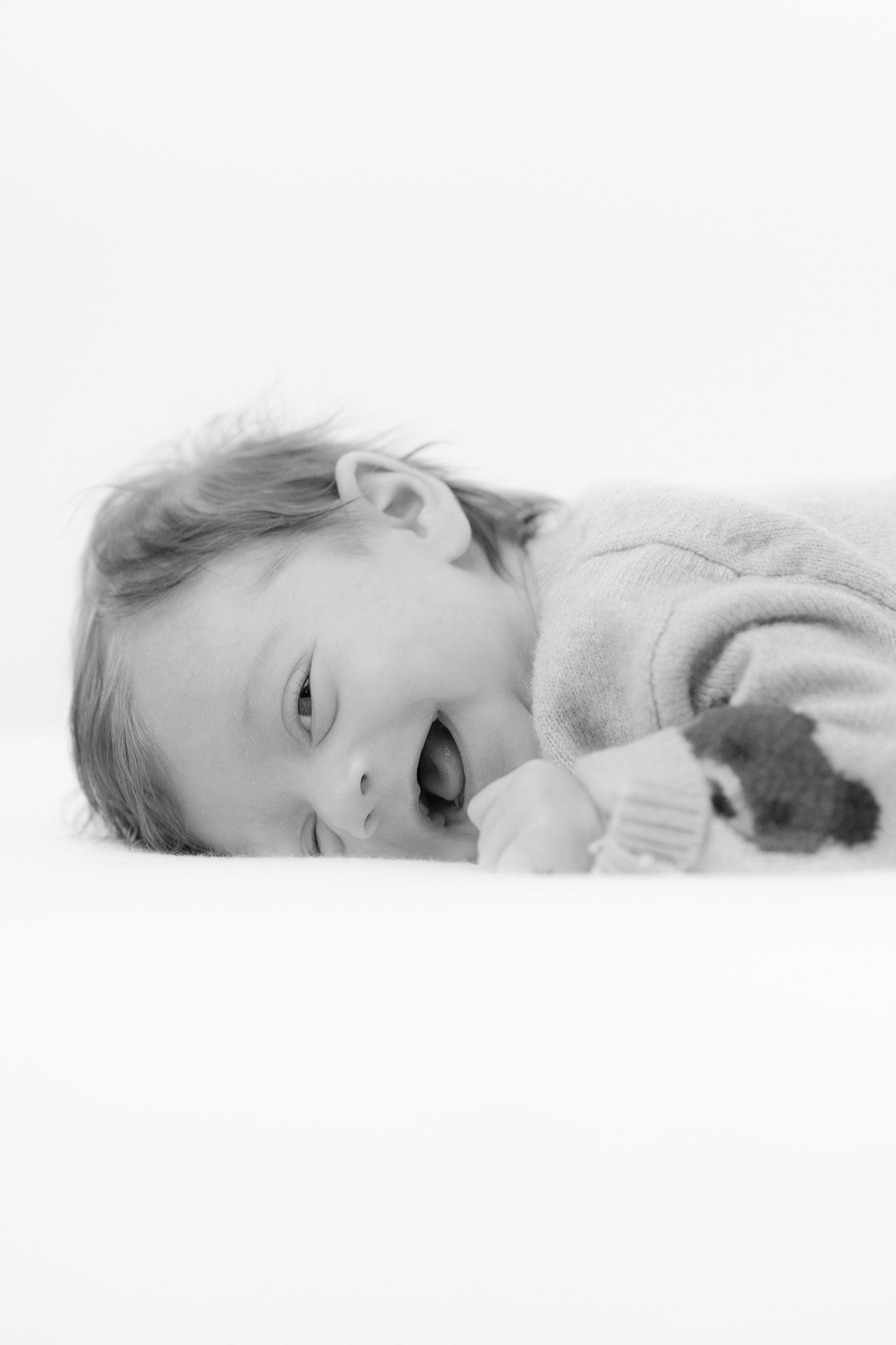 Ein kleines Baby liegt auf dem Bauch, zur Seite gedreht und lacht fröhlich. Schöne schwarz-weiß Newborn-Fotografie.