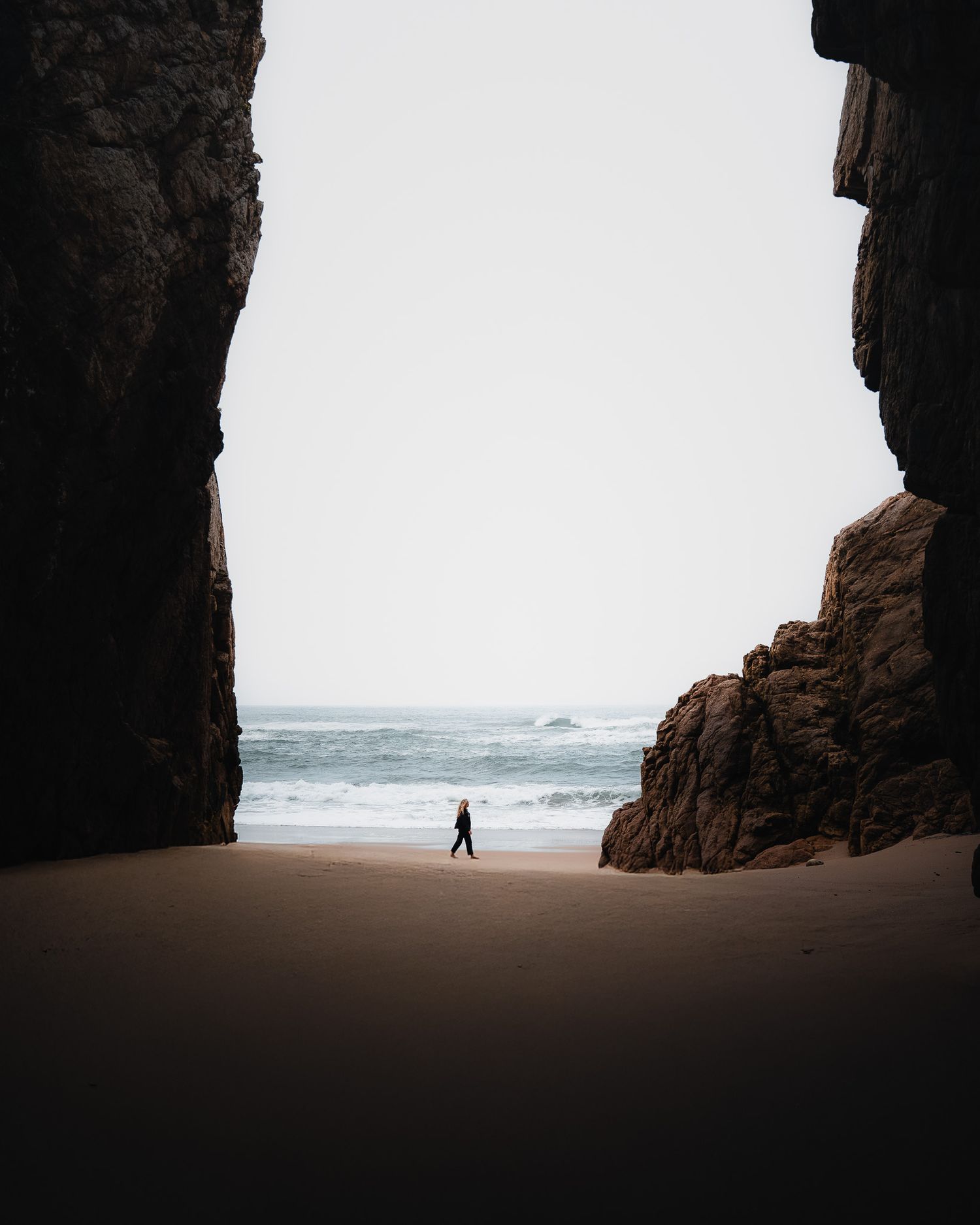 Ein Strandabschnitt in West-Portugal, umrahmt von zwei Felswänden, in der Mitte eine Frau die durchs Bild läuft.