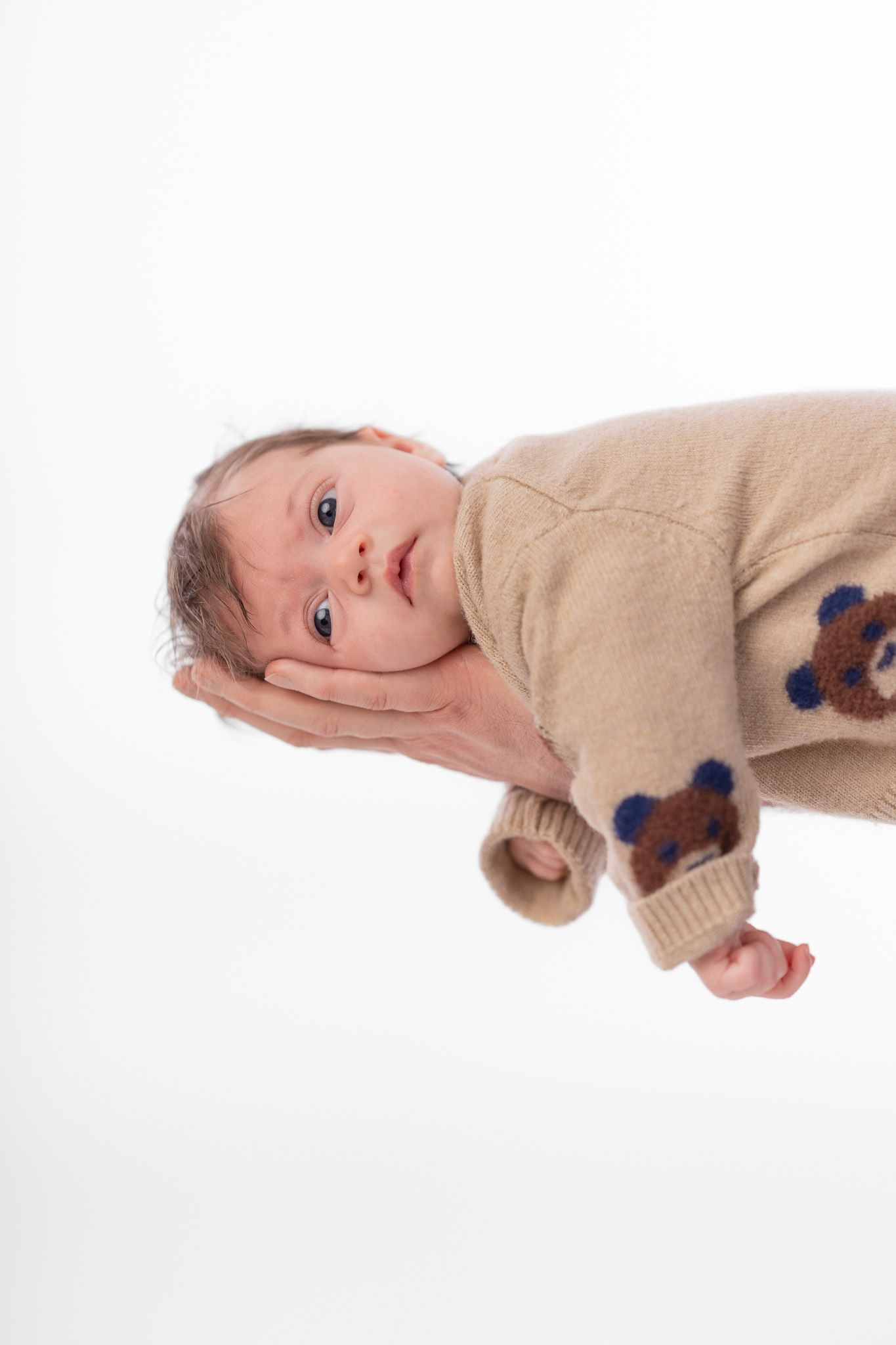 Ein Neugeborenes liegt auf dem Unterarm des Vaters und schaut in die Kamera, die Arme hängend. Süße Idee für ein Newborn Portrait.