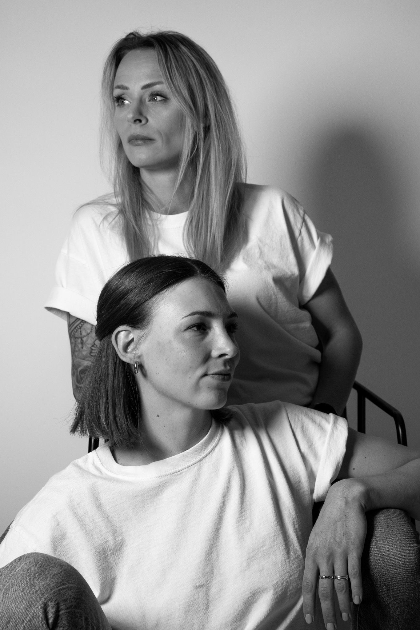 Zwei Frauen sitzen lässig versetzt voreinander und schauen in entgegengesetzte Richtungen. Moderne schwarz-weiß Portrait Aufnahme.