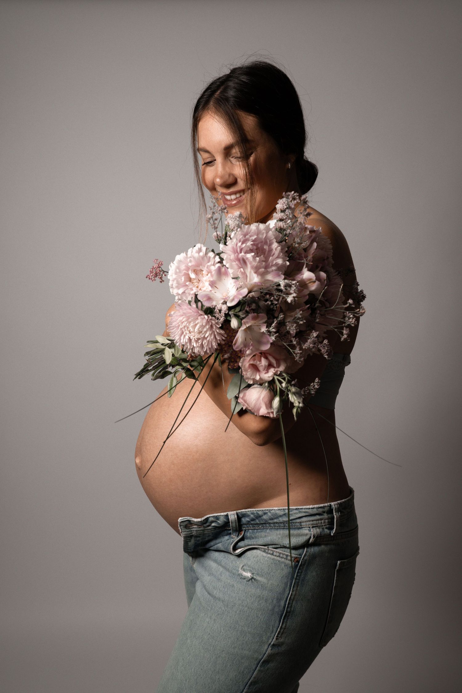 Ein Portrait von einer Schwangere Frau, die auf ihren Babybauch hinunter schaut und dabei einen prachtvollen Blumenstrauß im Arm hält.