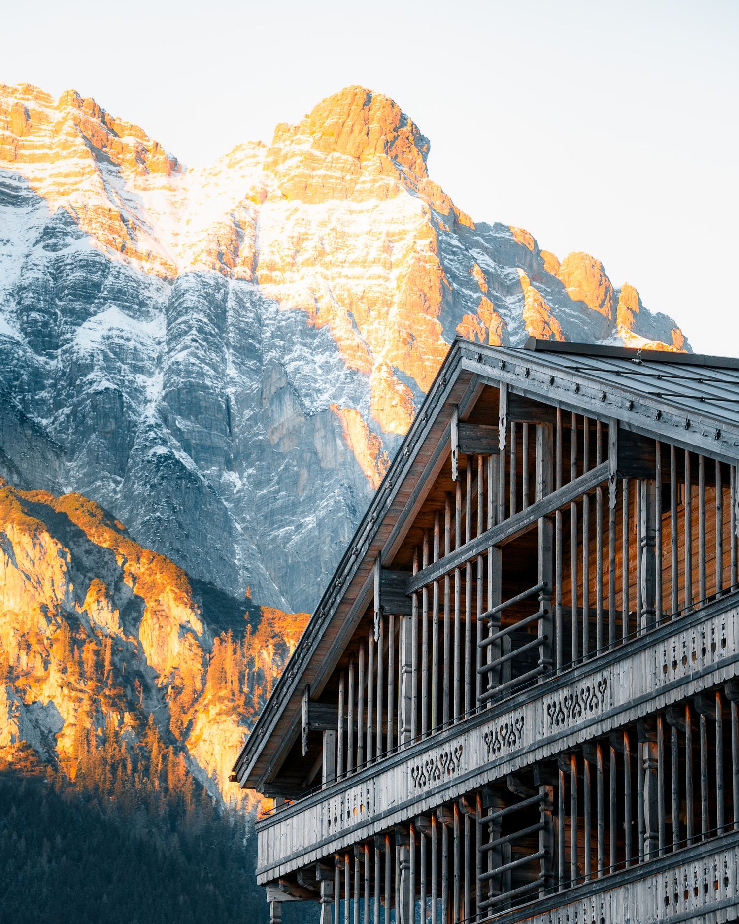 Berggipfel werden eindrucksvoll von der Abendsonne angestrahlt. Im Vordergrund die dekorative Holzfassade eines Hotels.