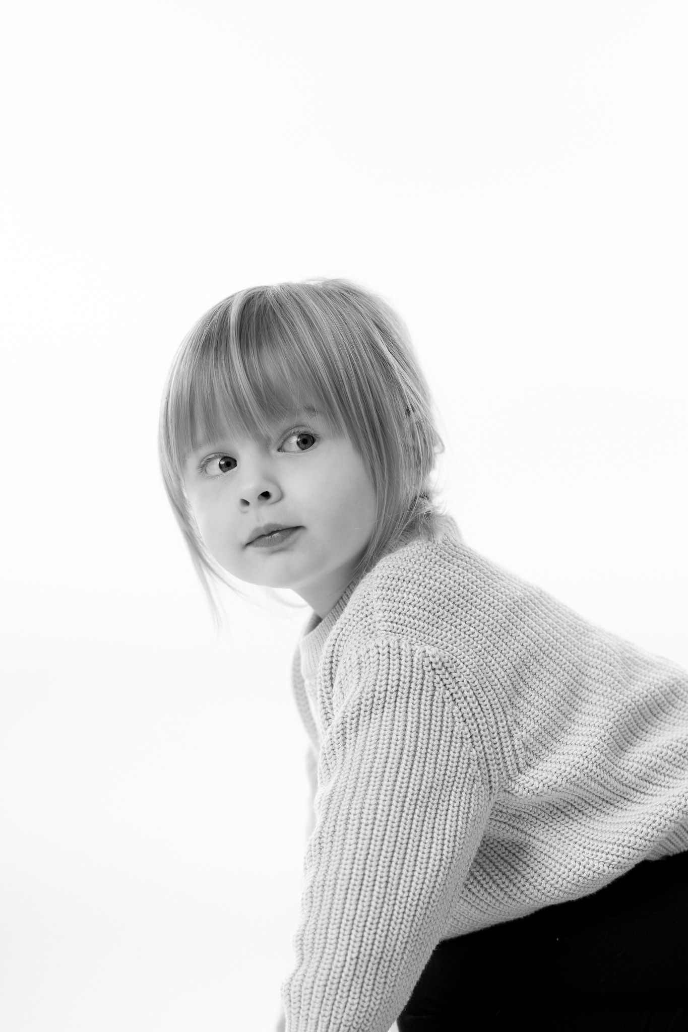 Ein Kleinkind schaut verschmitzt über die Schulter. Schwarz-weiß Portraitfotografie.