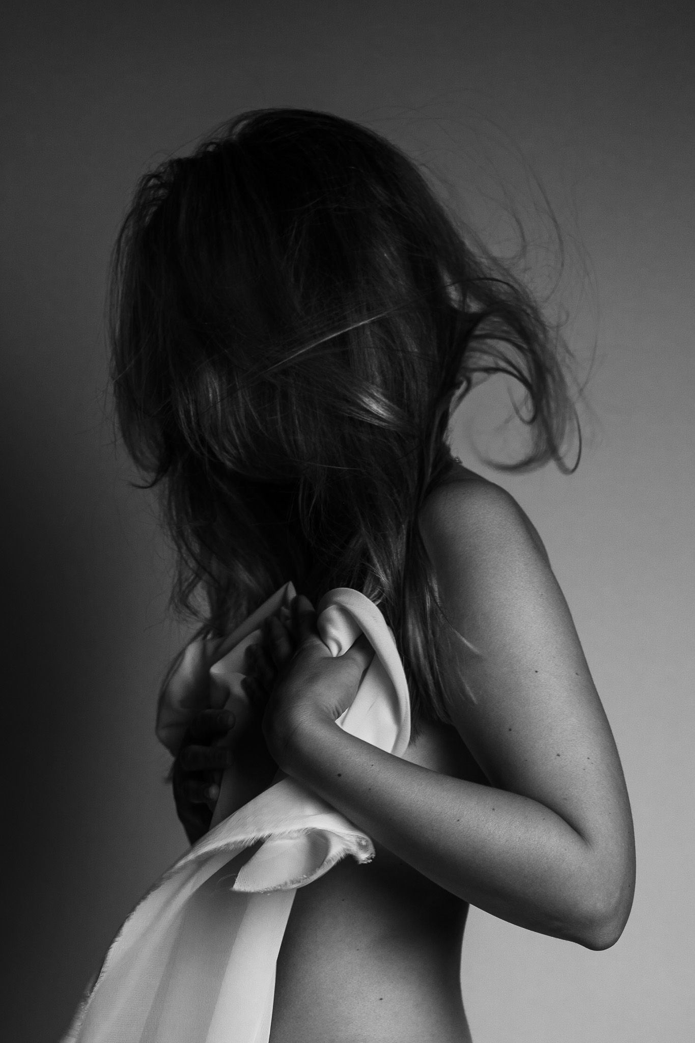 schwarz-weiß Profil von einer jungen Frau mit wilden langen Haaren, die sich eine weiße Decke vor die Brust hält um sie zu bedecken.