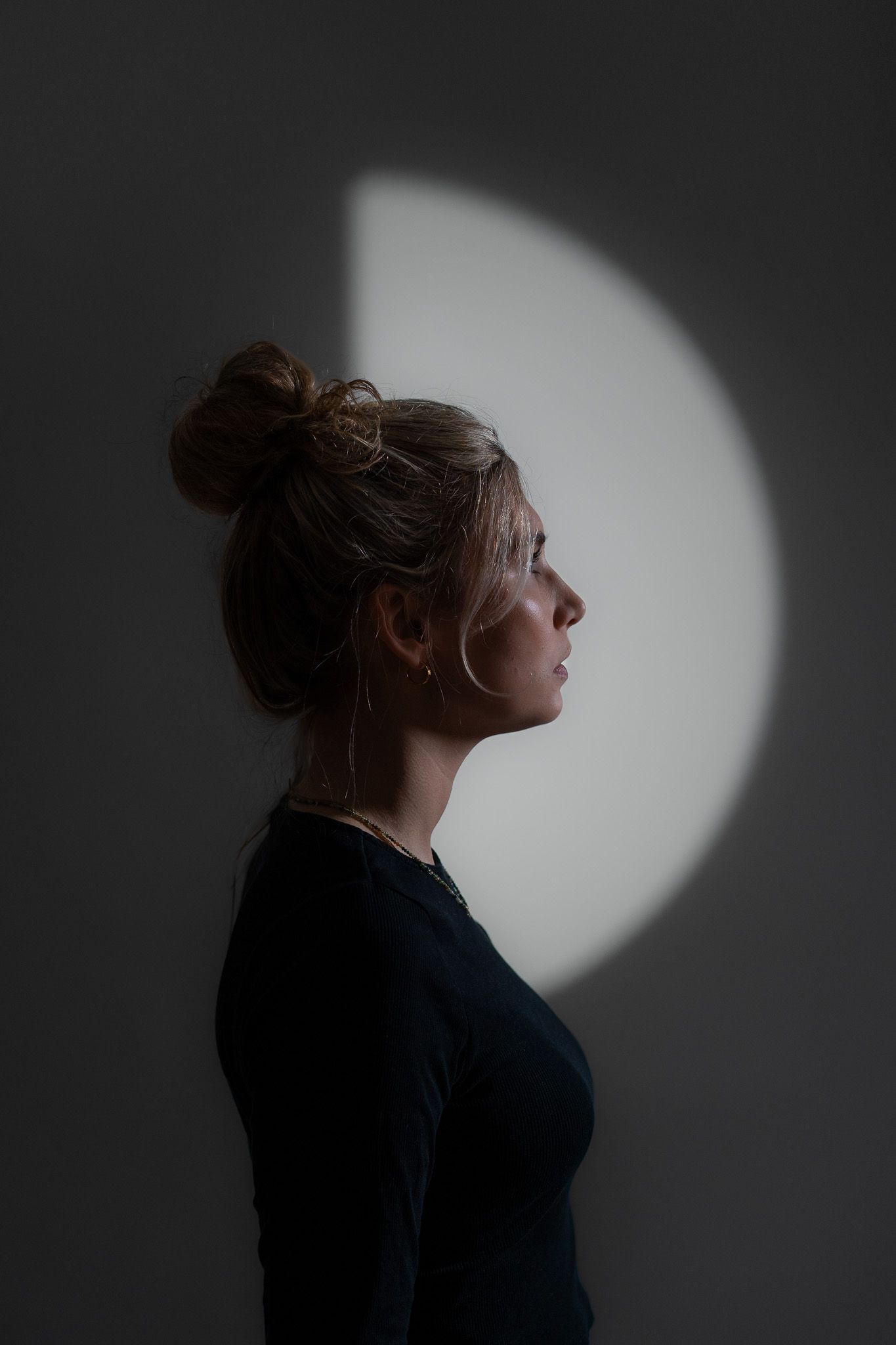 Künstlerisches Portrait vom Profil eines Gesichts einer jungen Frau. Spiel mit Licht und Schatten. Im Hintergrund ein Halbkreis aus Licht.