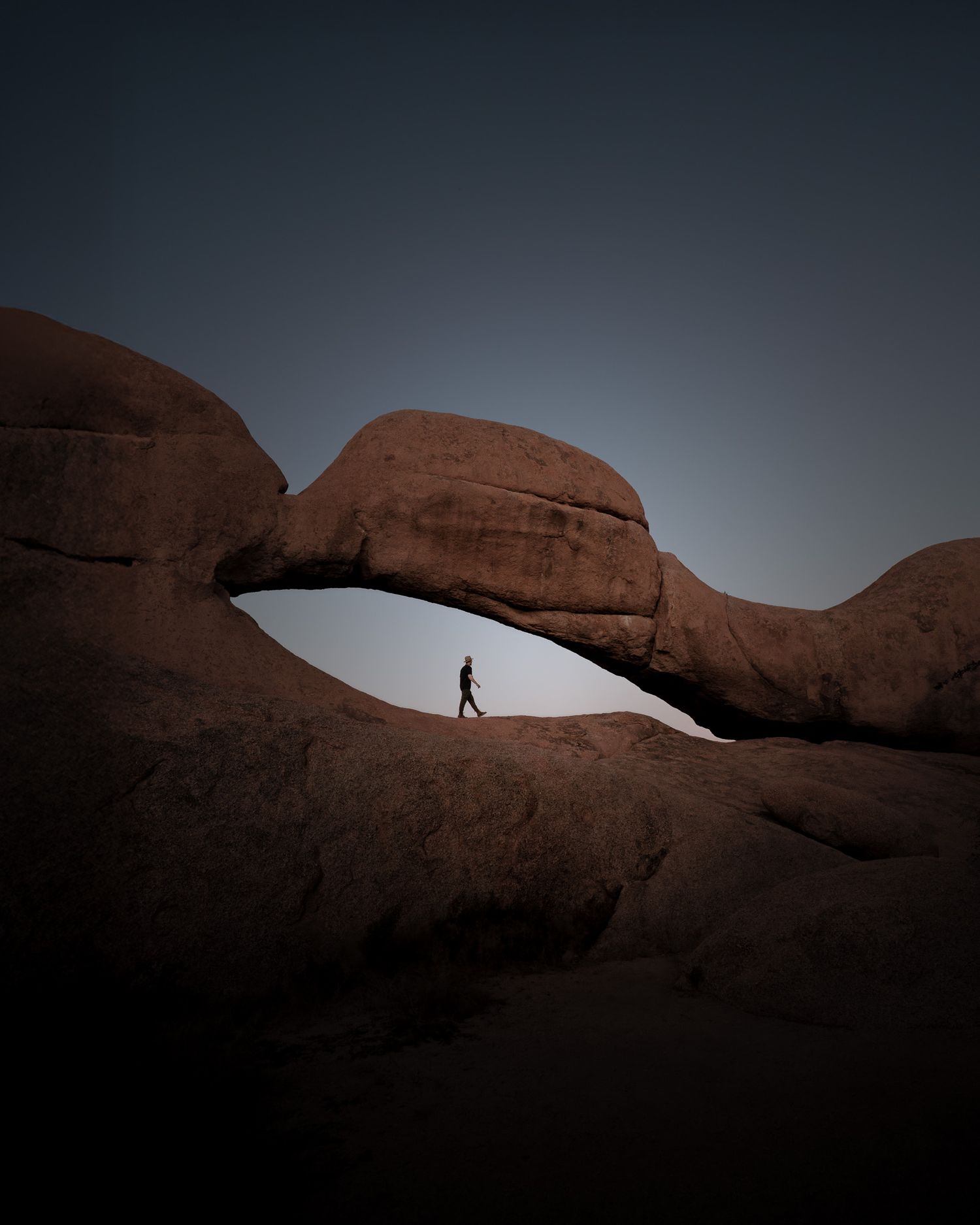 Ein Steinbogen bei Dämmerung in Spitzkoppe, Namibia. Ein Mann geht hindurch.