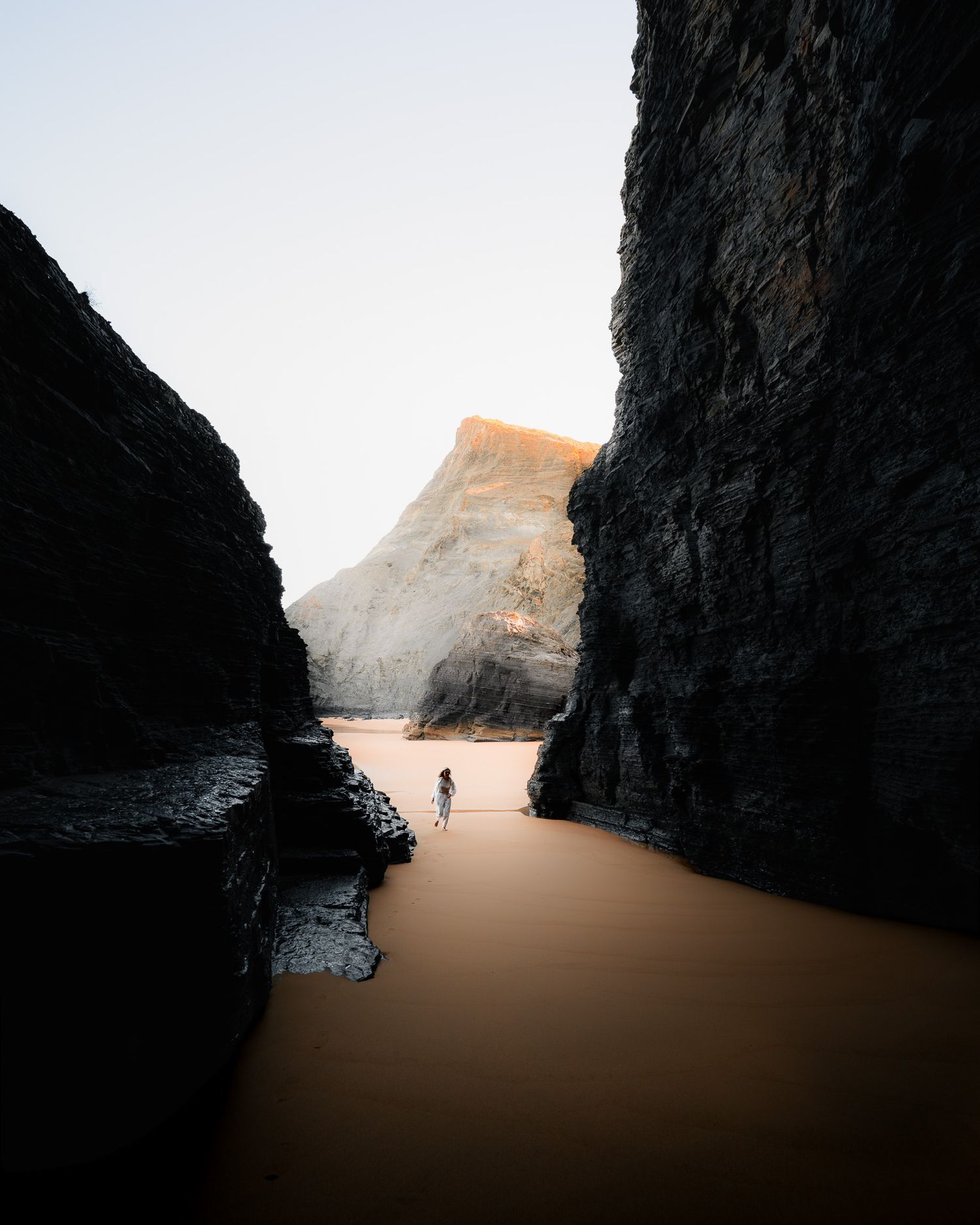 Ein interessanter Strandausschnitt aus einer Höhle heraus fotografiert. Weiß gekleidete Frau. Tolle Farbabstimmung und Linienführung.