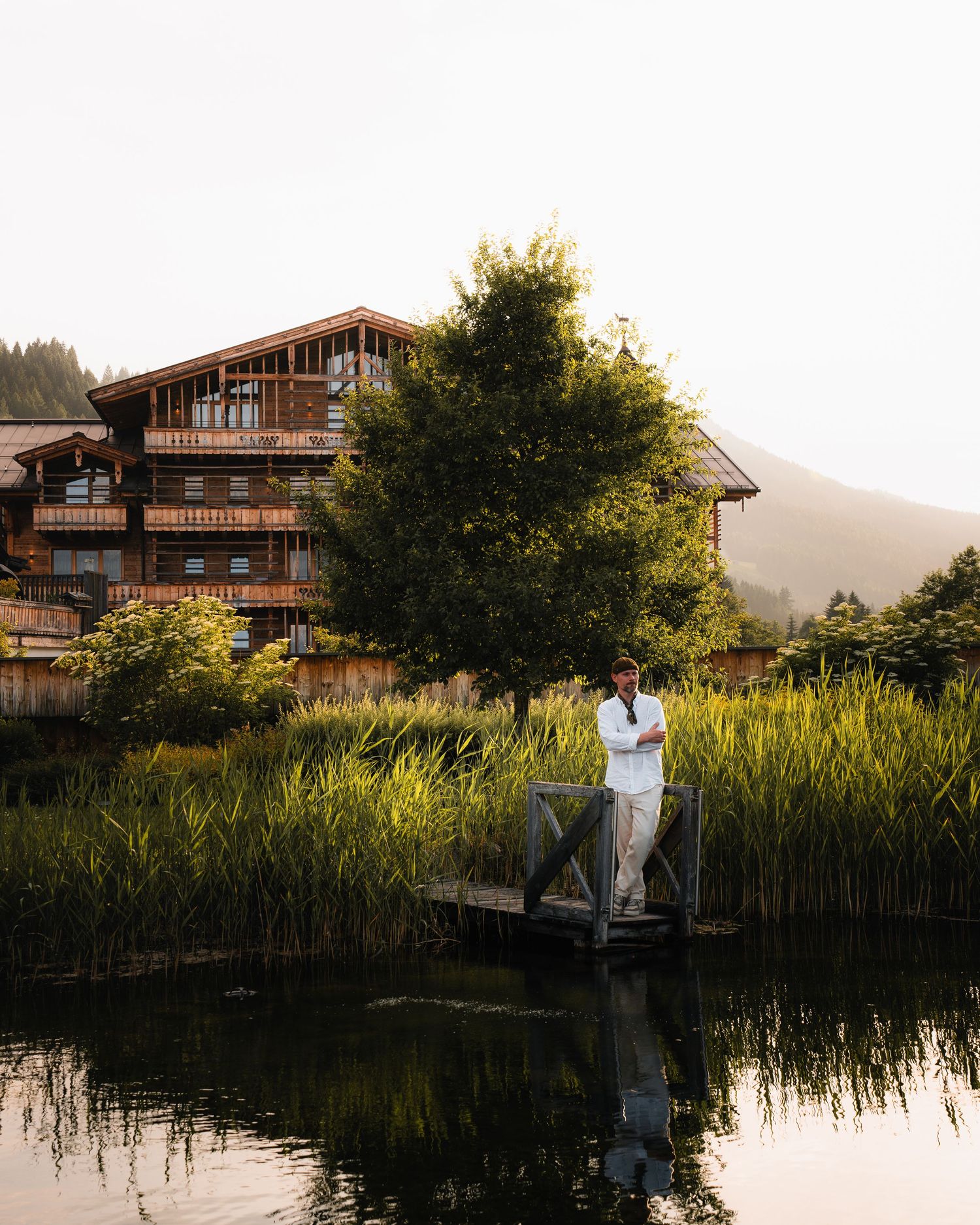 Ein lebendiges, farbenfrohes Bild. Ein Mann steht auf einem Steg und schaut auf einen See. Hotelinszenierung. Hochzeitslocation.