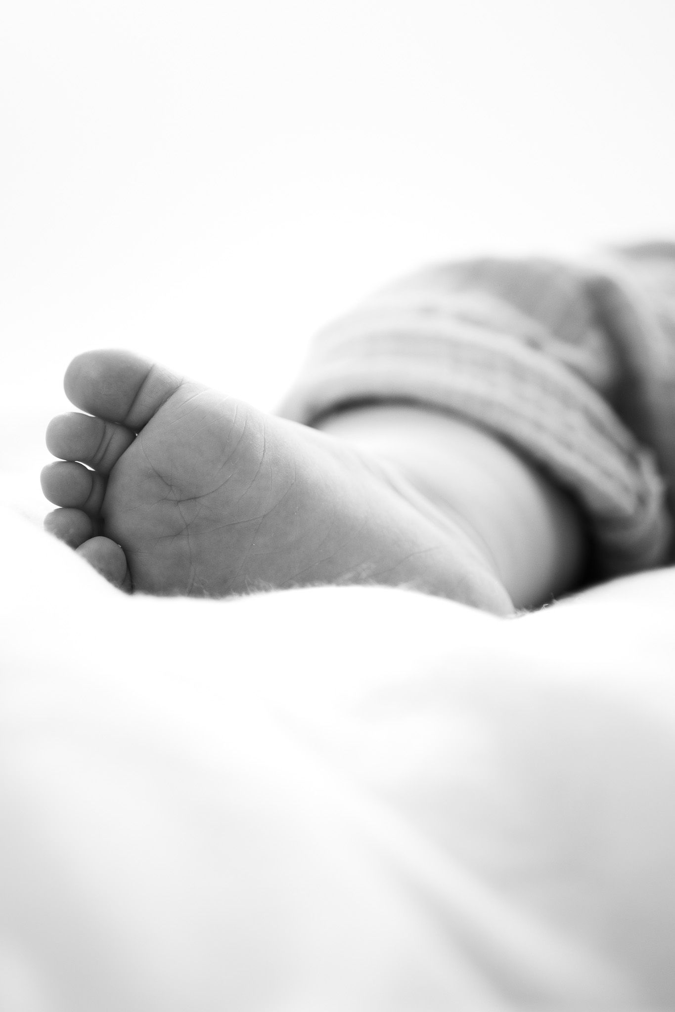 Eine Detailaufnahme von einem kleinen Babyfuß der auf einer hellen Decke liegt. High Key Fotografie.