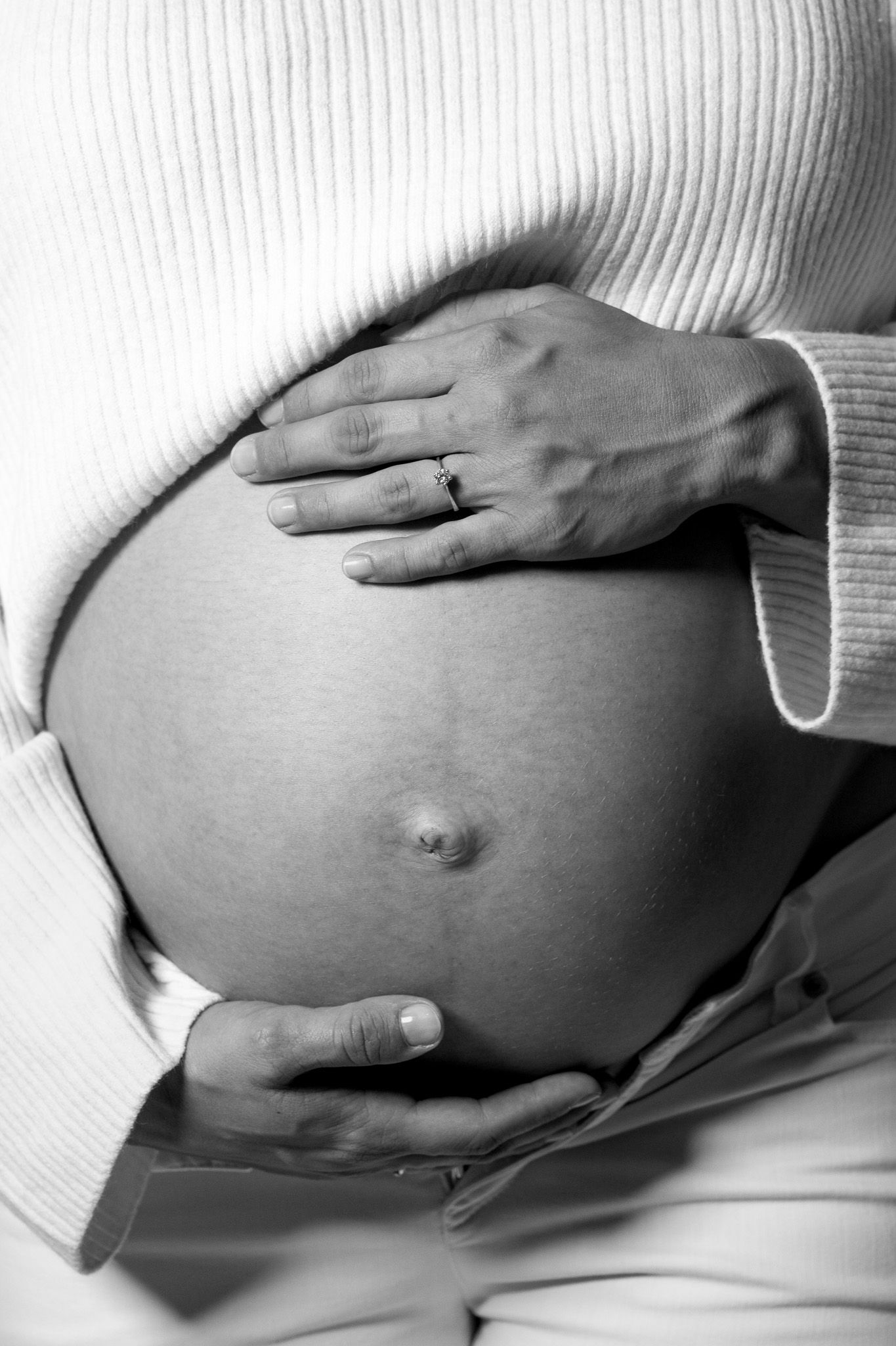 Ein schwarz-weiß Foto von einem Babybauch. Die Schwangere umfasst liebevoll ihren Bauch. Ästhetische Schwangerschaftsfotografie Baden-Baden.