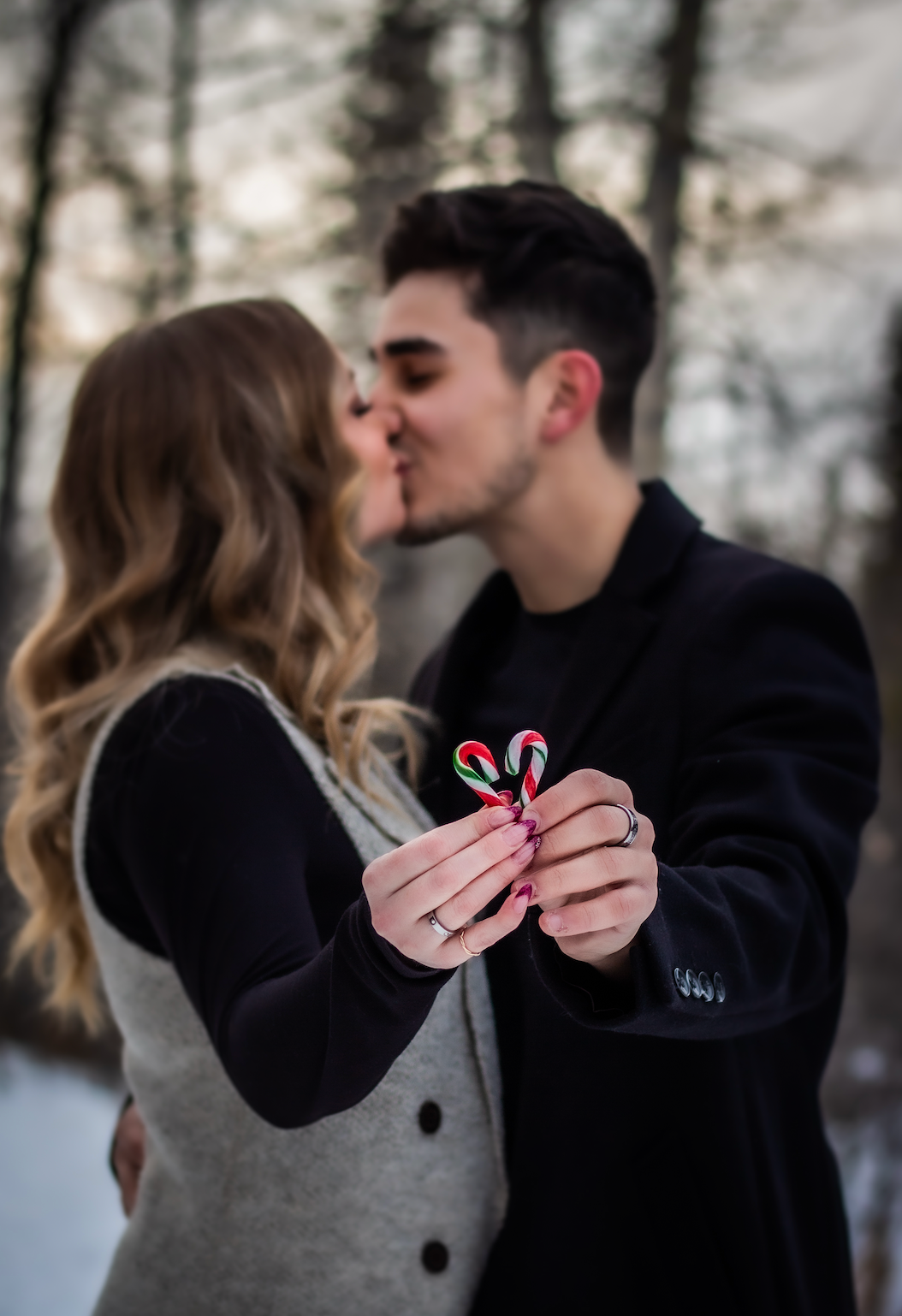 couple kissing while holding up two candy canes in a heart shape