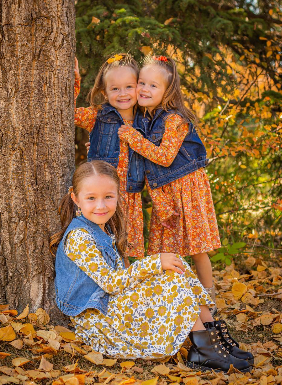 Three sisters huddled hugging under a autumn tree smiling