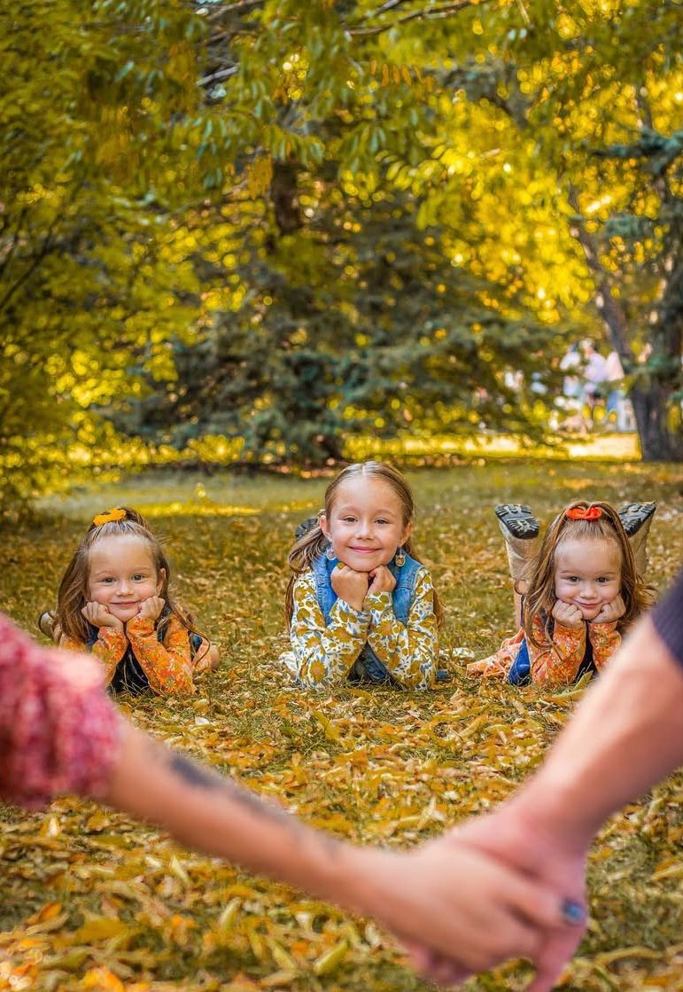 Three children laying on their tummy with hands under chin. Parents holding hands in front of them