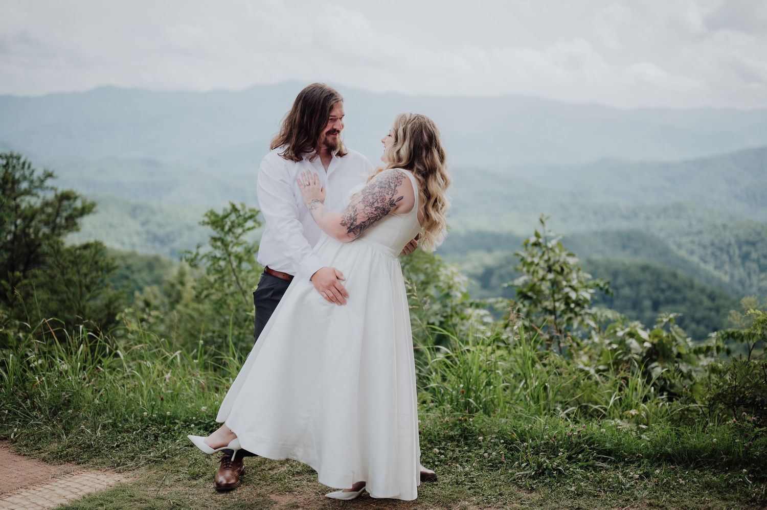 Bride and groom share a romantic moment with lush green mountain views in the background.