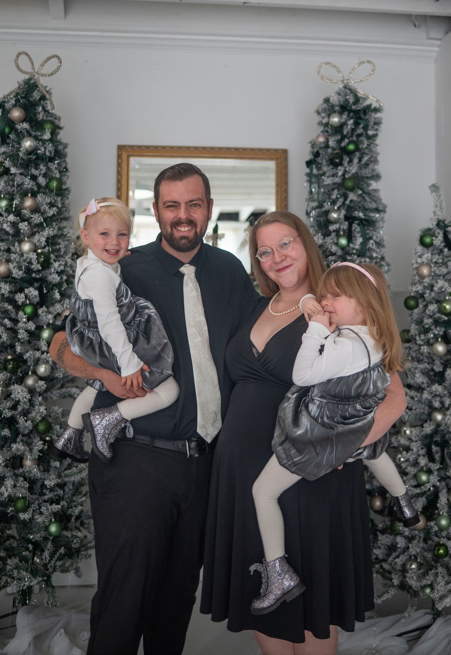A formal family portrait in front of decorated Christmas trees with silver and white ornaments.