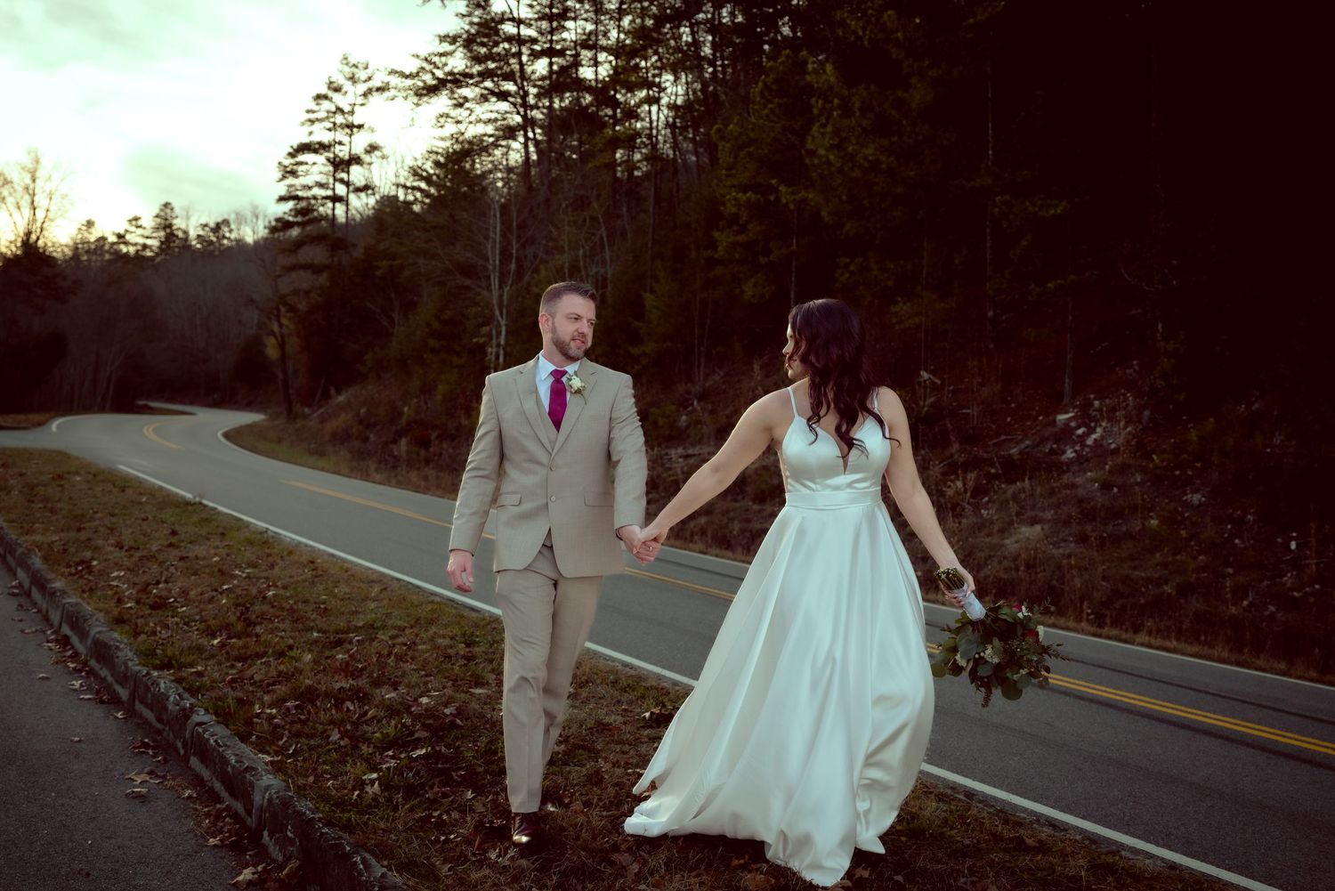 Wedding couple walking along a scenic mountain road at sunset.