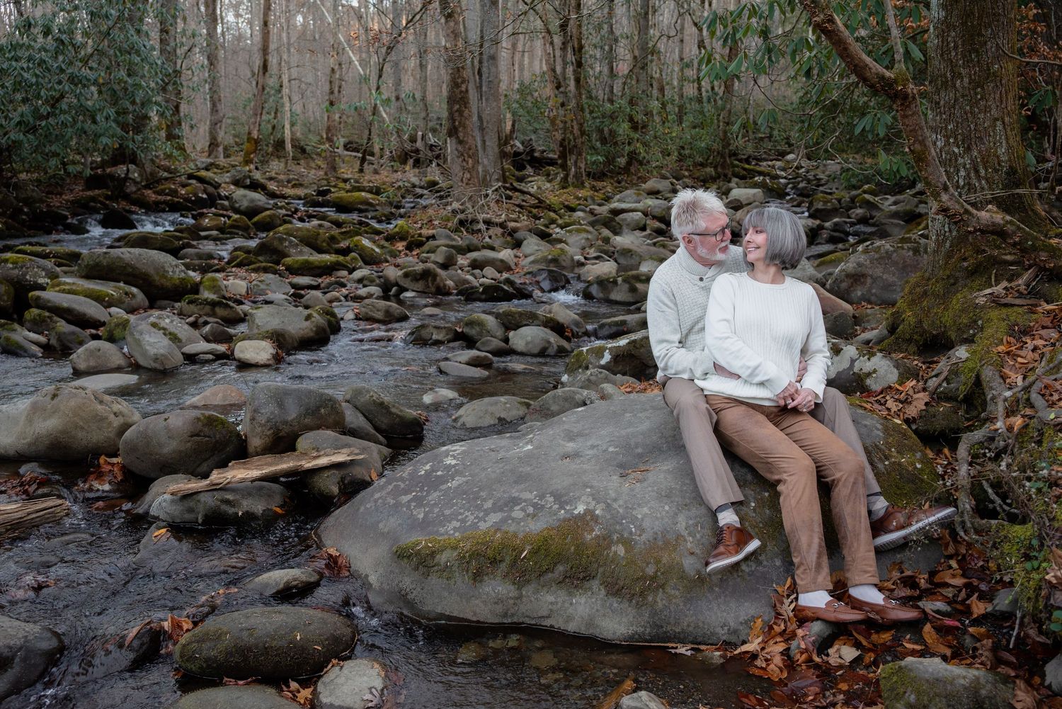 Couple sitting together on rocks by a peaceful stream in nature.