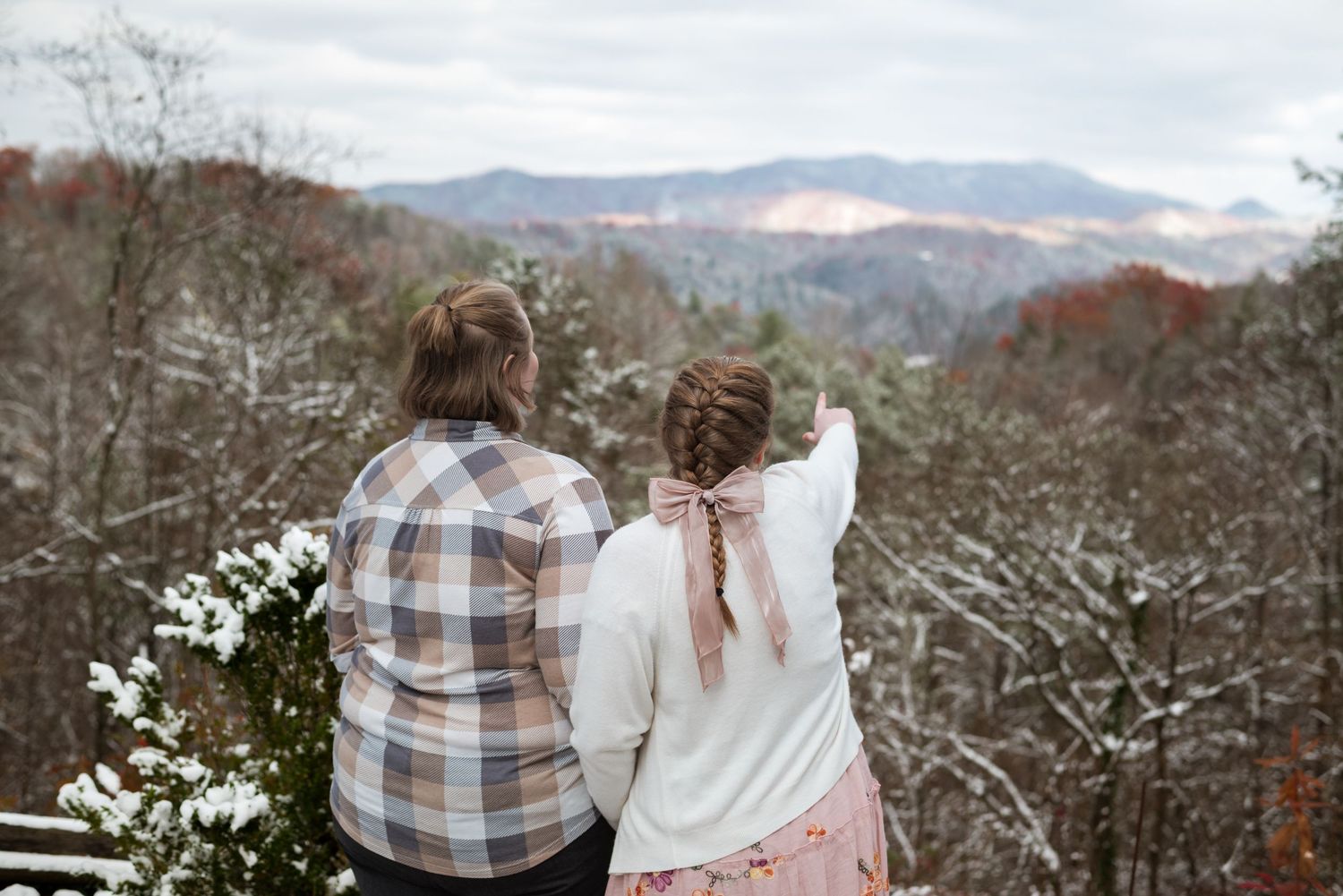 Couple in plaid and white outfits walking together through a misty mountain landscape.