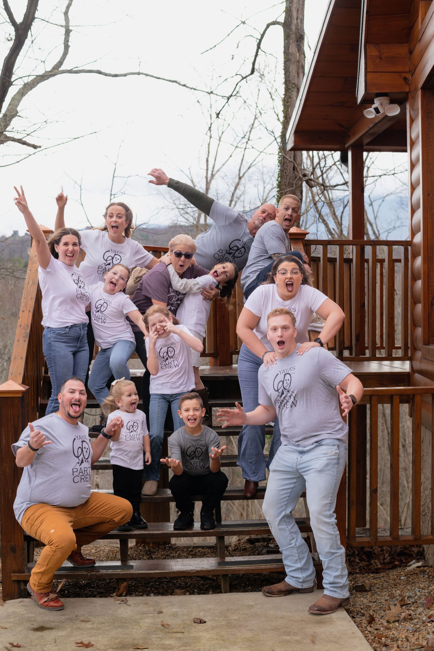 Group wearing matching gray shirts posing energetically on a wooden deck with mountains in the background.